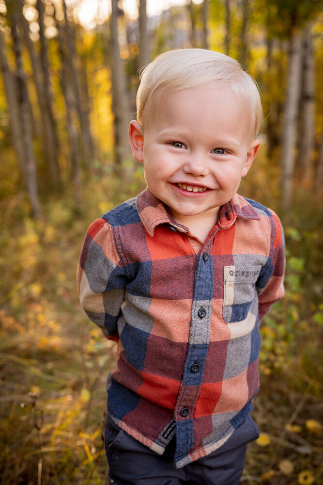 a little boy in a blue and red plaid shirt gives a huge smile at the camer