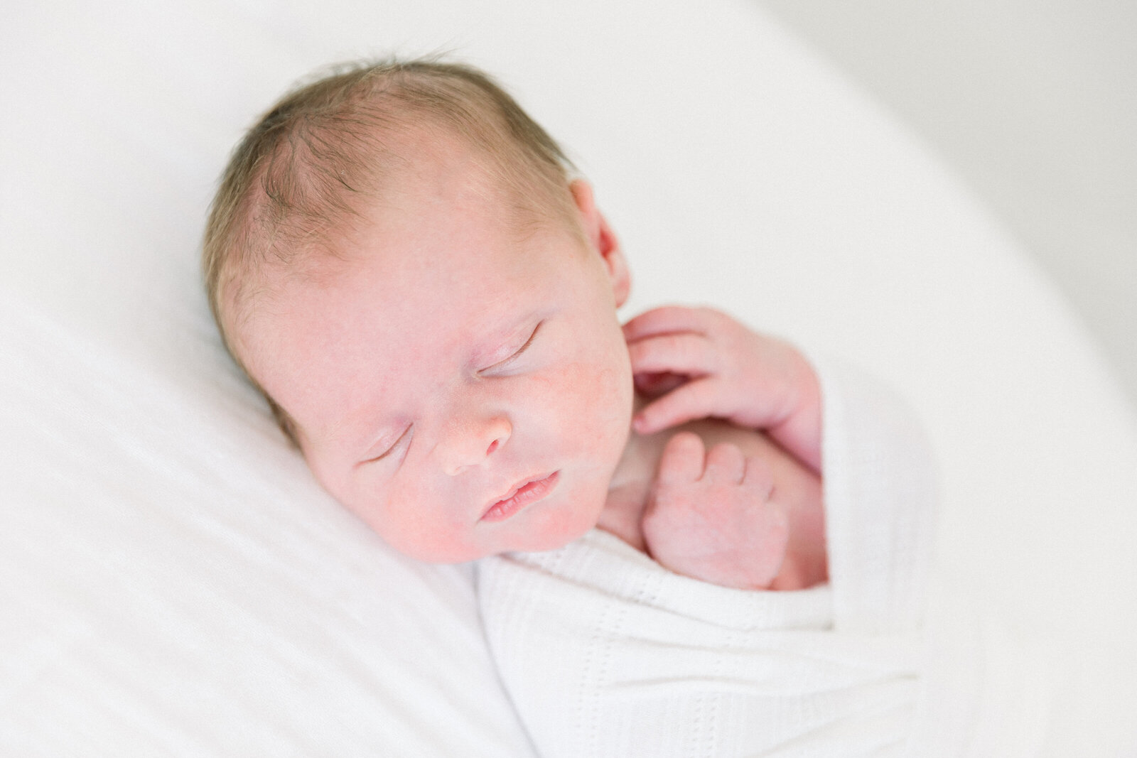 Image of newborn baby wrapped in white with hands showing sleeping taken by Newborn Photographer Sacramento Kelsey Krall