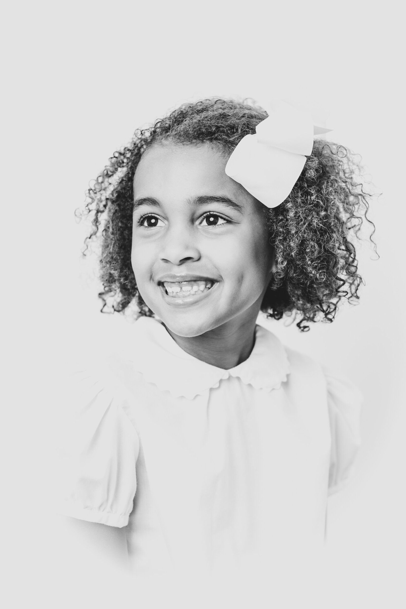 Young girl with curly hair smiles off camera during heirloom portrait session in Raleigh NC