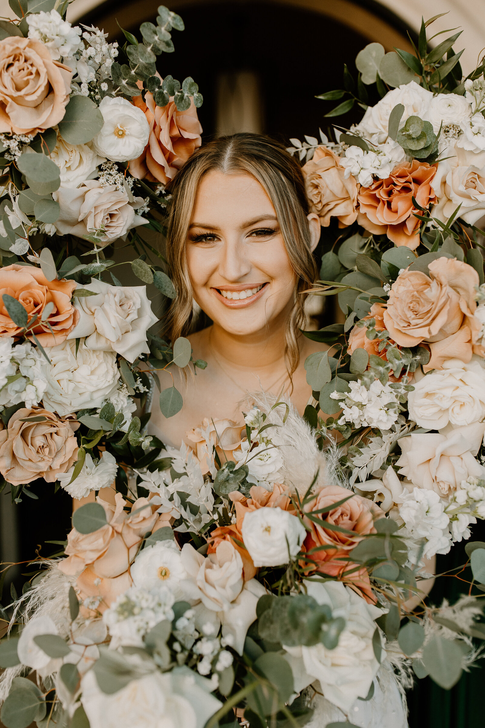 A bride smiling with bouquets of flowers all around her head.