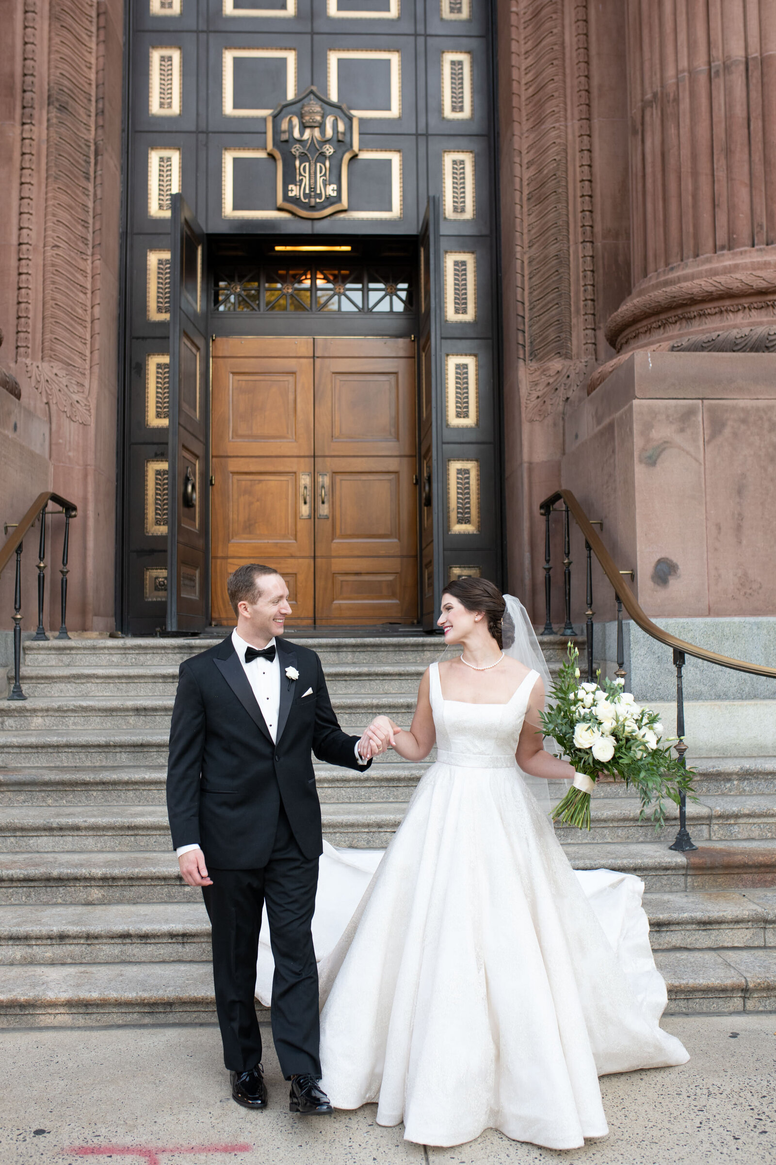 A bride and groom stand in front of a catholic church.