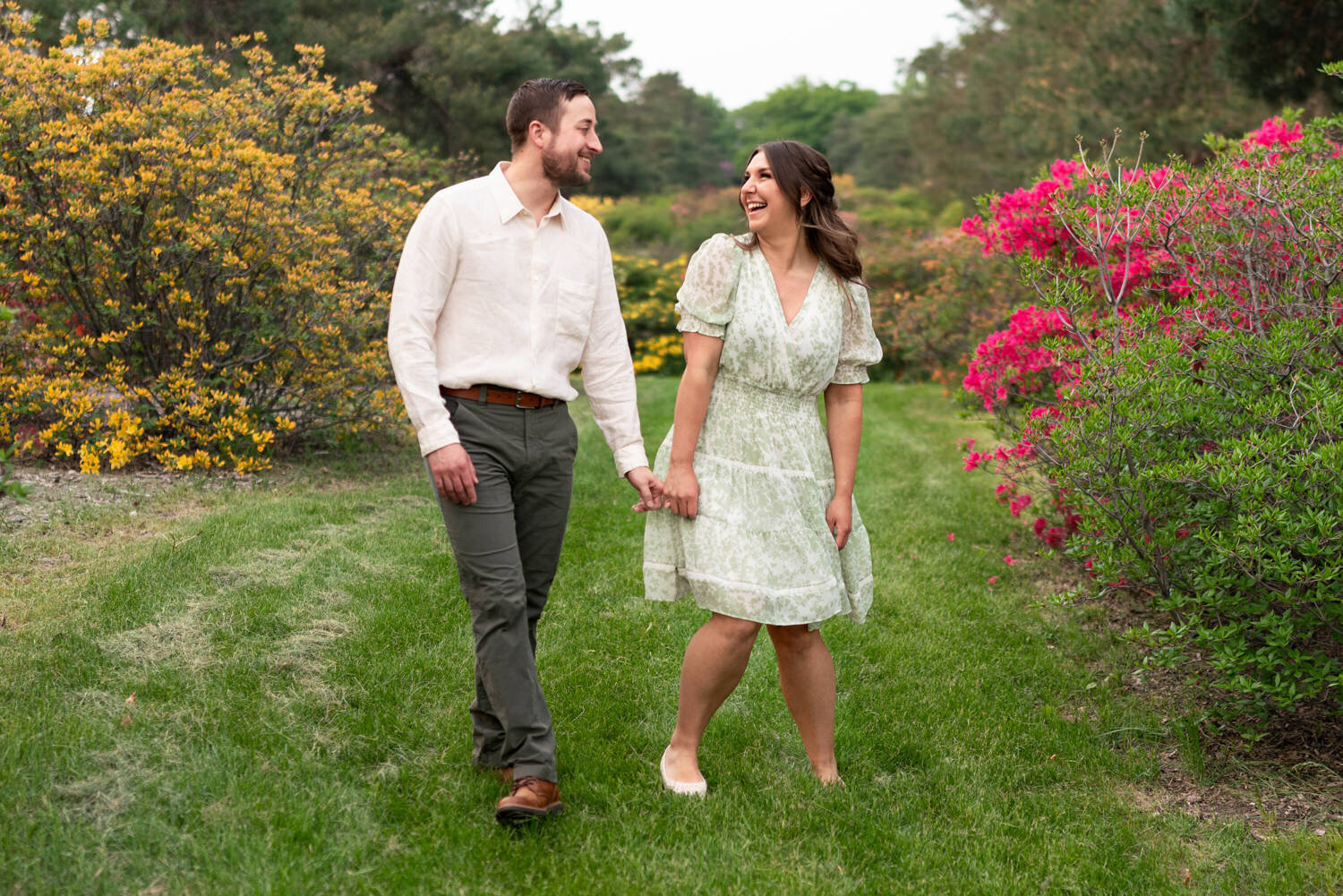 Man and woman laugh while walking through a garden of flowers.