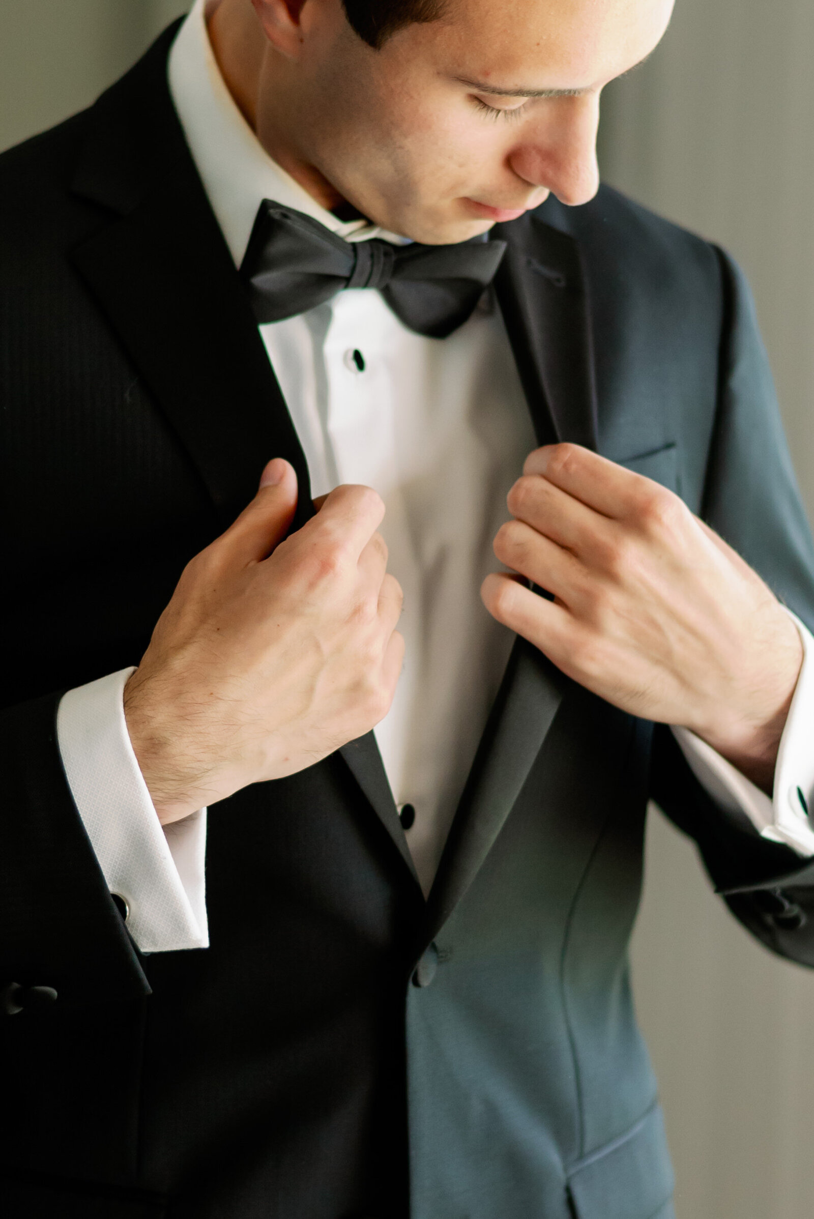 Groom adjusting his tuxedo jacket lapels while looking down toward his hands