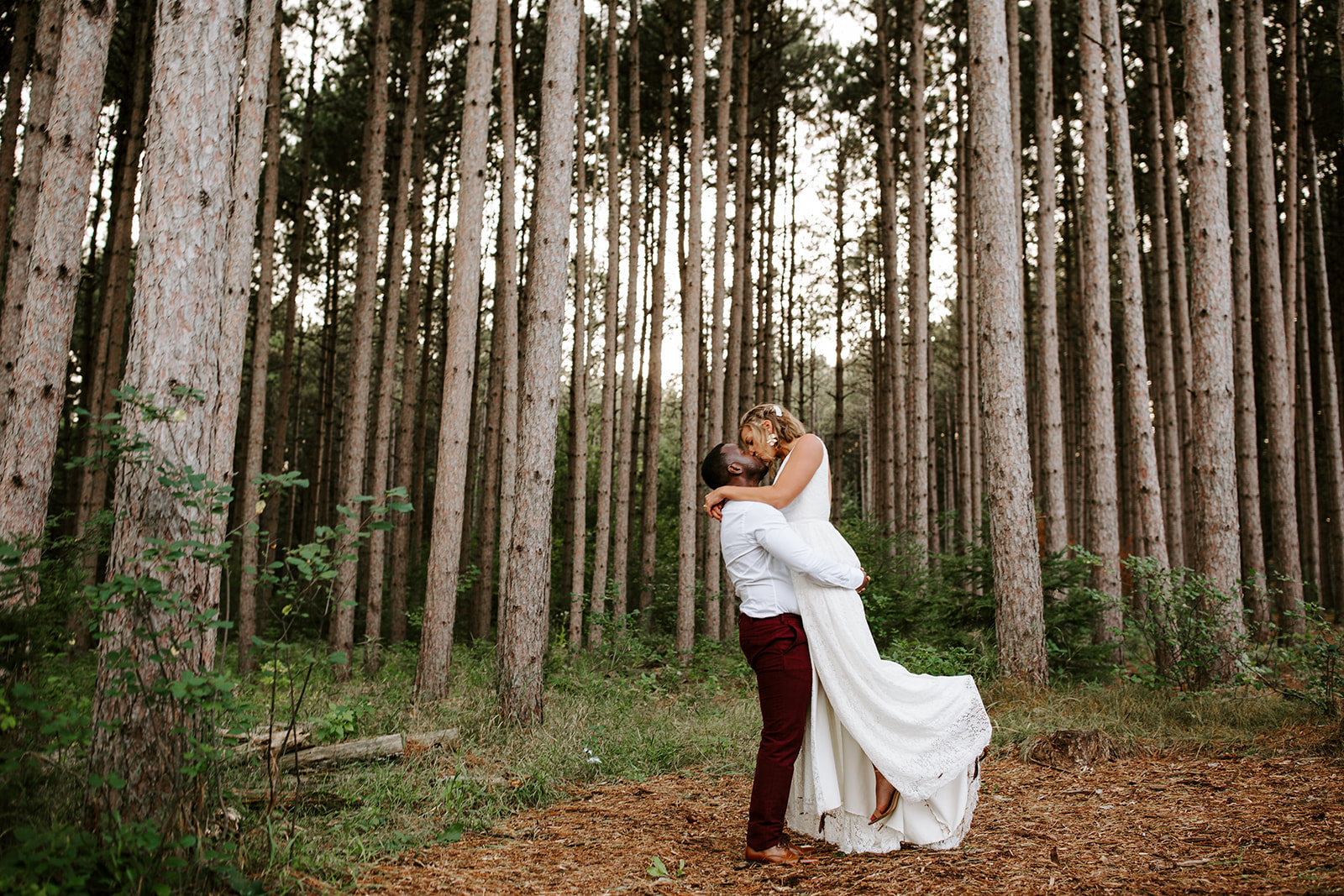 Groom lifting his bride kissing in tall pine tree at Pinewood Wedding Venue