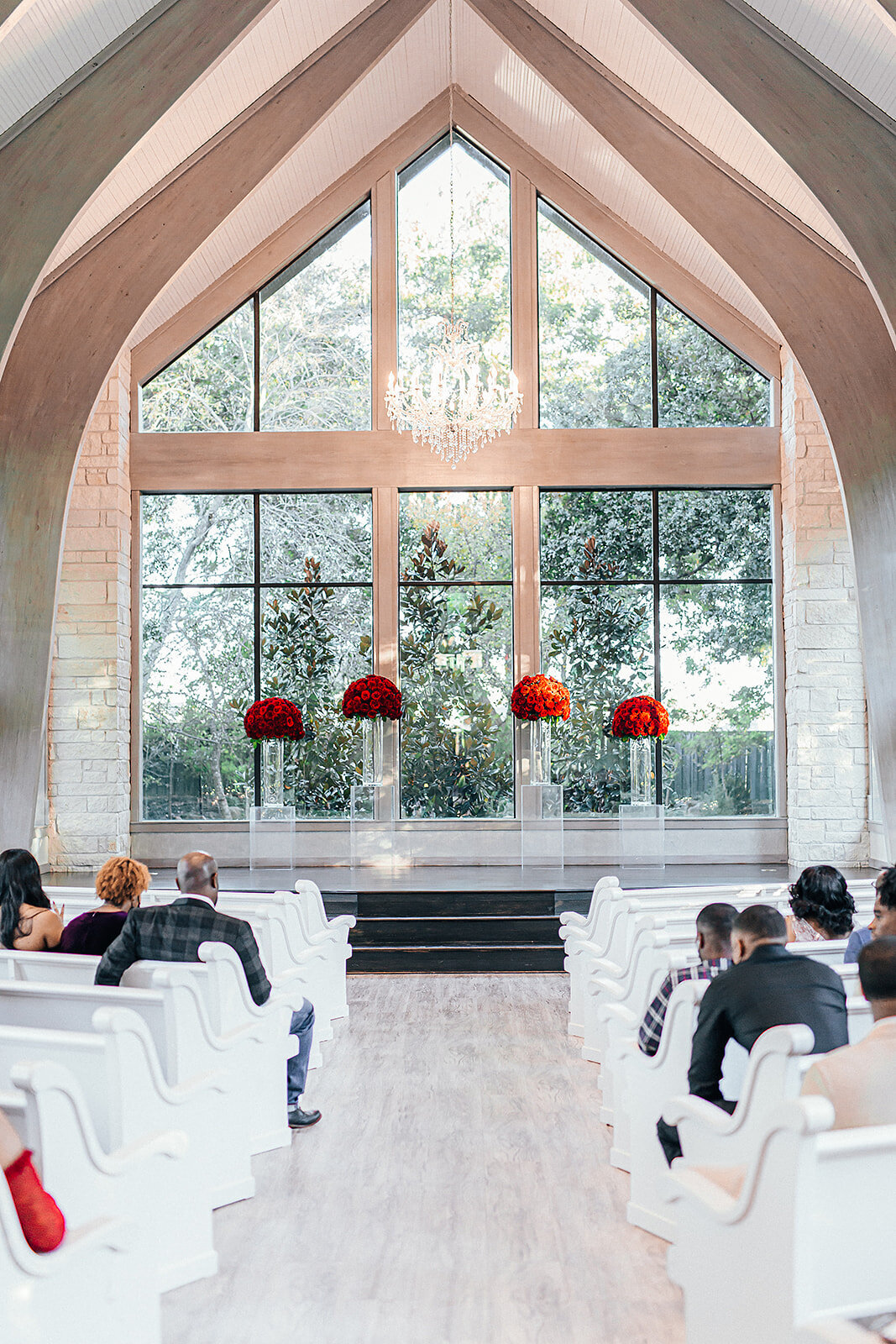 Church aisle for wedding ceremony with large window and red flower arrangements