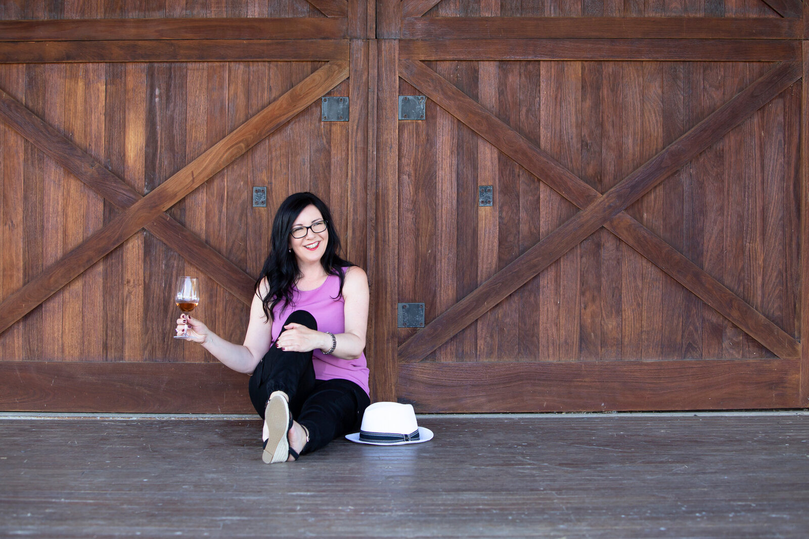 lady sitting on ground in front of barn doors hold a glass of wine