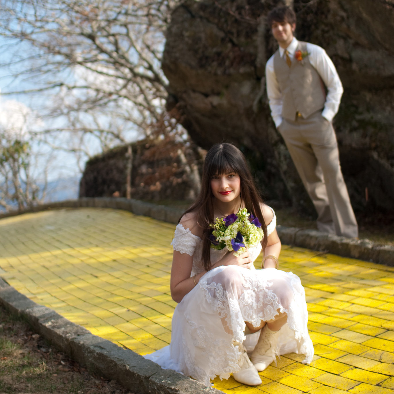 a pretty bride kneels down on the yellow brick road in front of a groom at land of oz