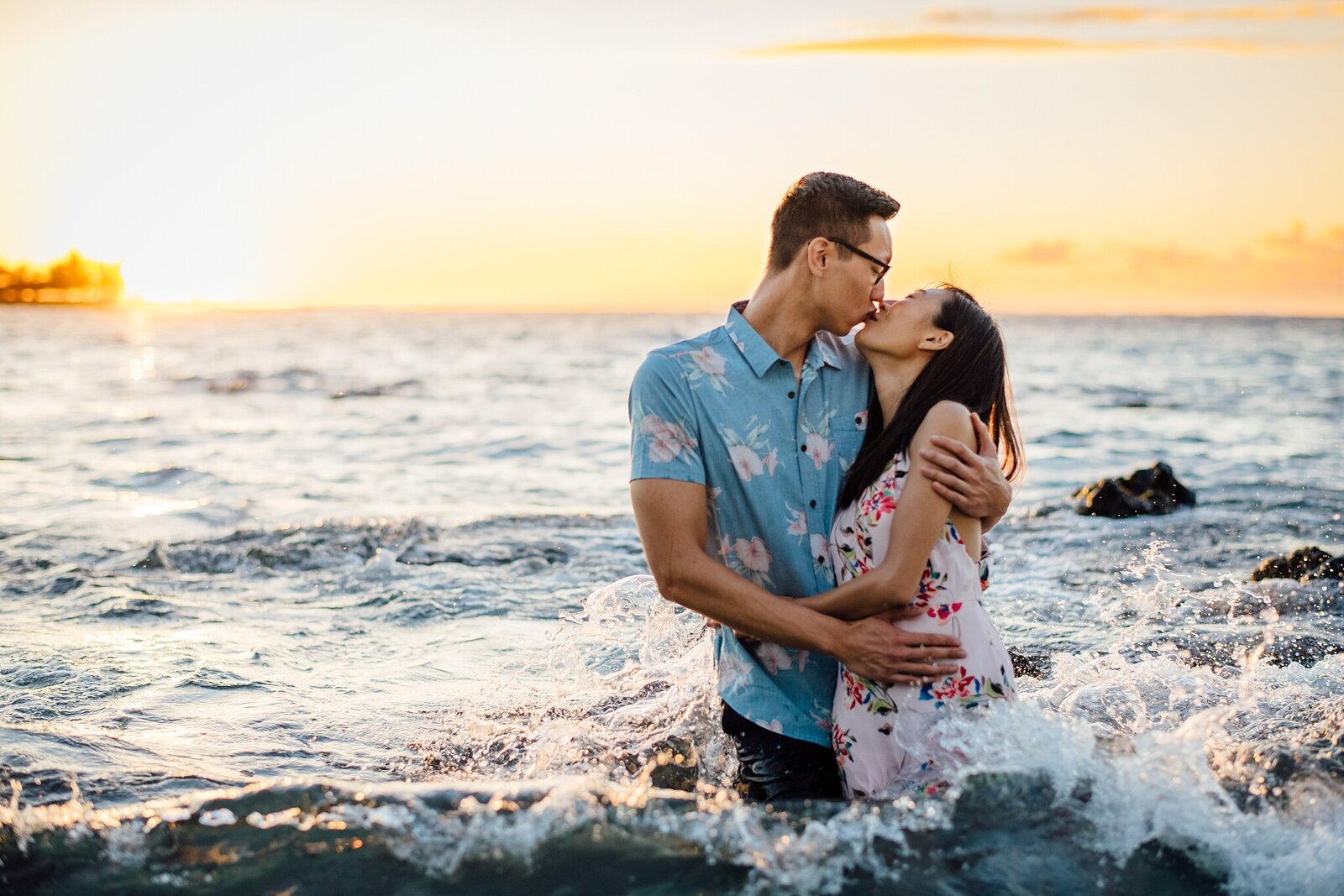 couples kiss as wave crash behind them