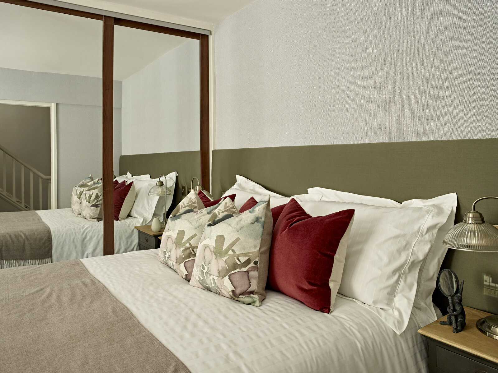 bedroom suite with mirrored wardrobe and maroon pillows on white bed.