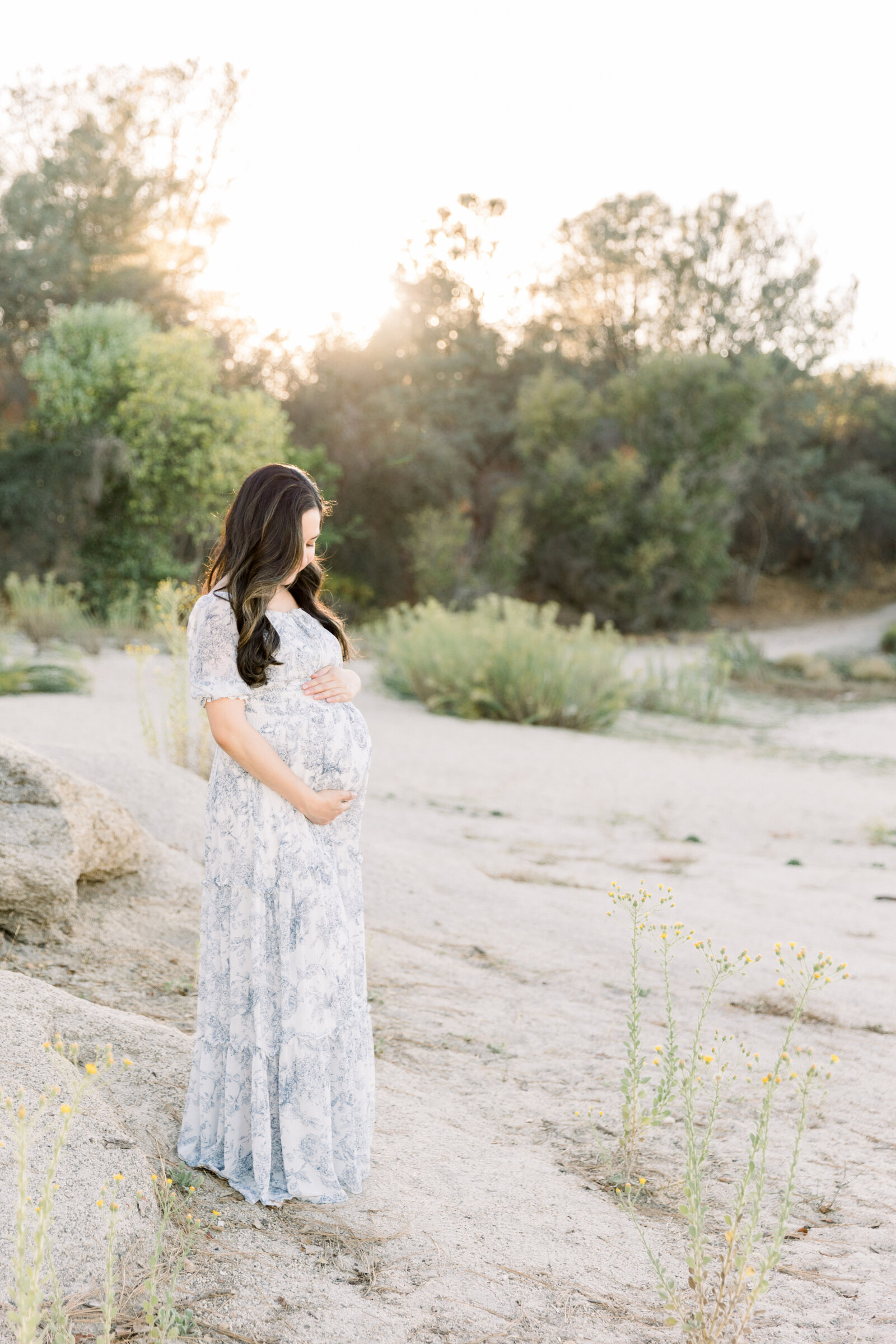 Image of expecting mother holding her belly standing on sand and rocks taken by Sacramento Maternity Photographer Kelsey Krall