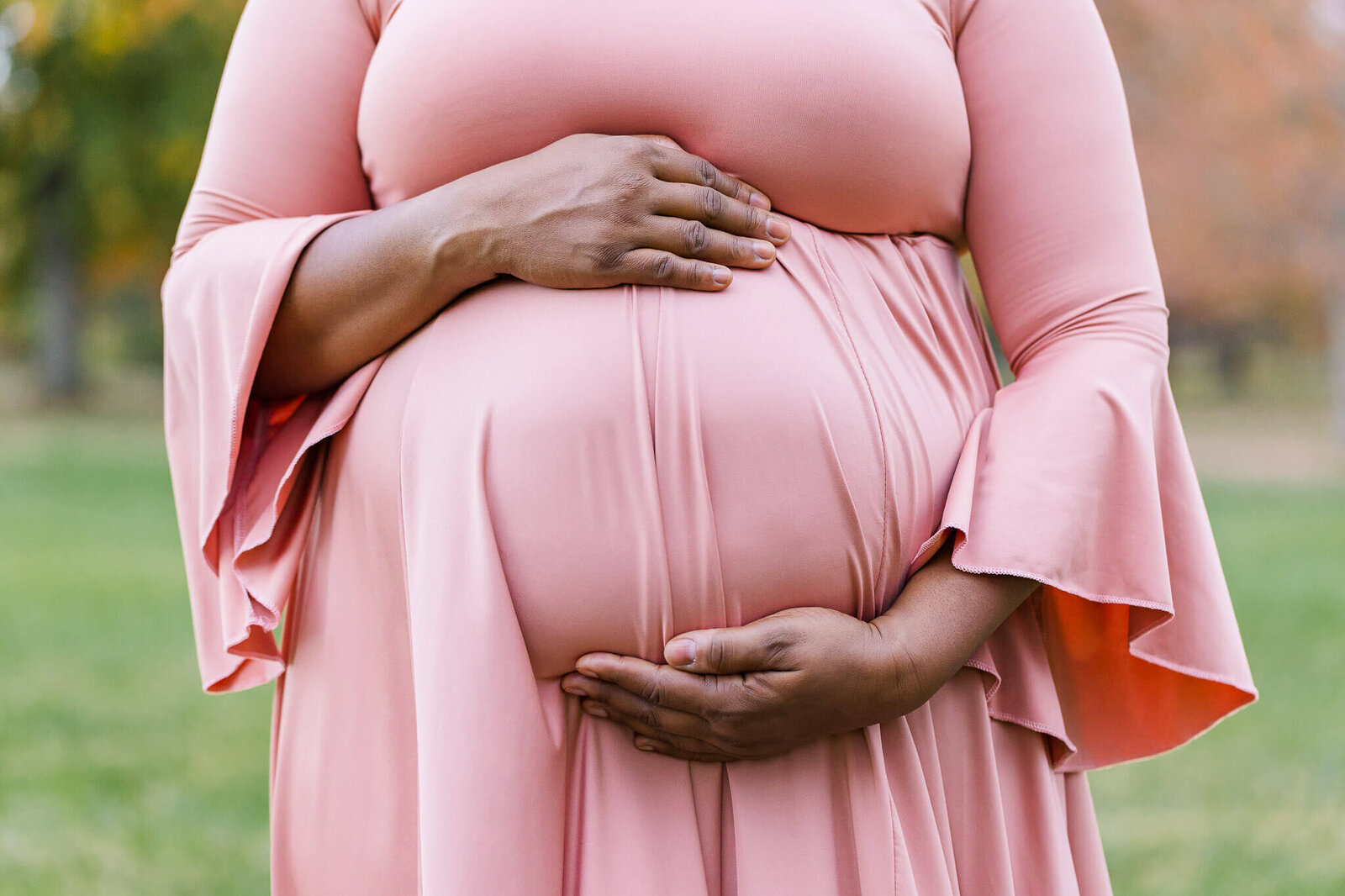 A close-up of a pregnant woman's belly in a pink dress.