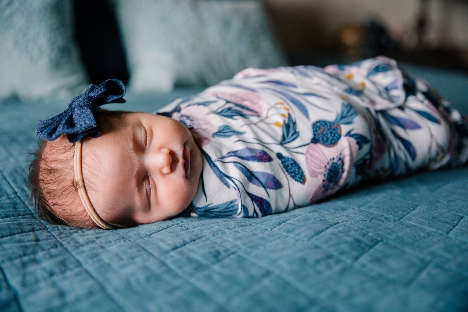 Newborn daughter in floral wrap lying on parent's bed during in-home photo session.