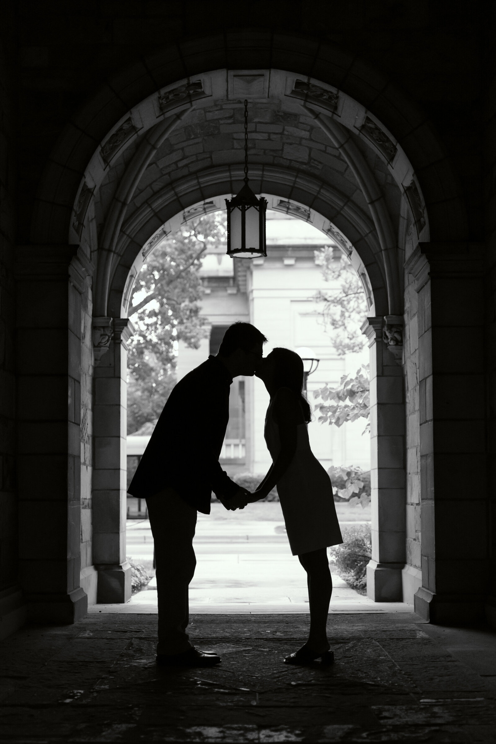 black and white photo of couple kissing in tunnel archway at university of michigan law quad
