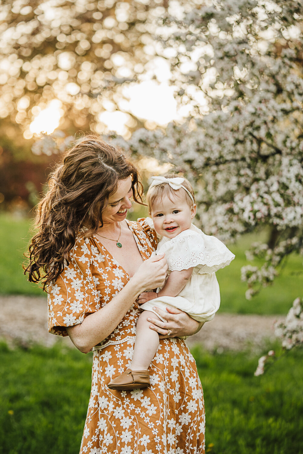 mother holds toddler girl at sunset with a flowering tree