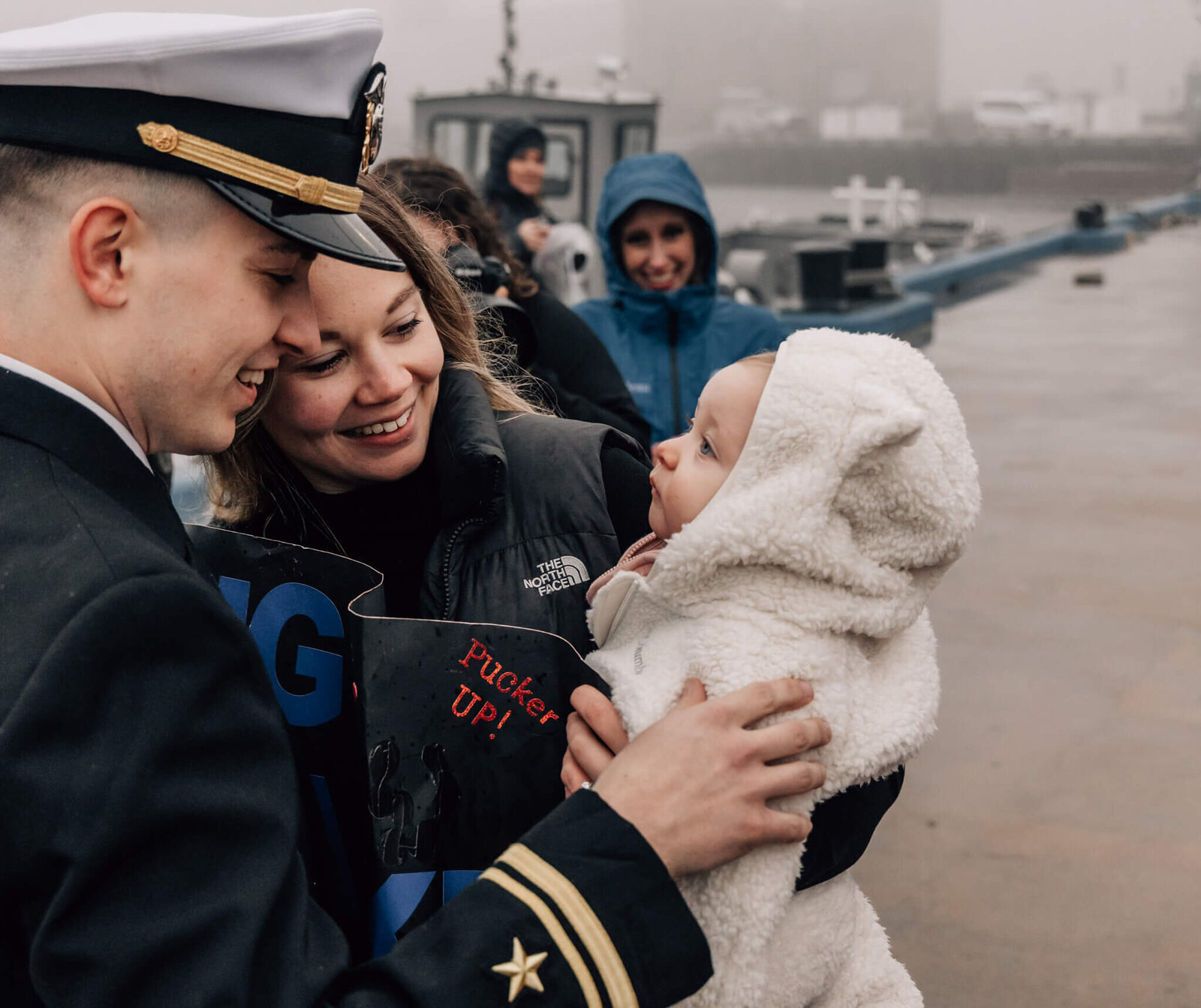 Naval officer and wife look at baby at homecoming of USS Newport News in Groton, CT.