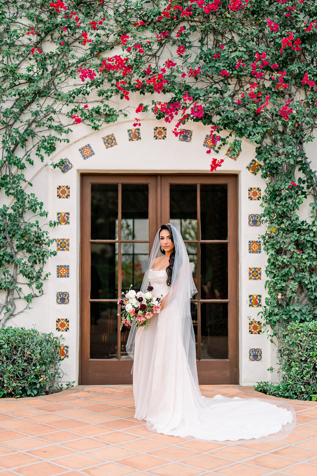 Bride standing before floral-covered arch in elegant gown, styled with editorial vision and photographed in film at Hummingbird Nest Ranch.