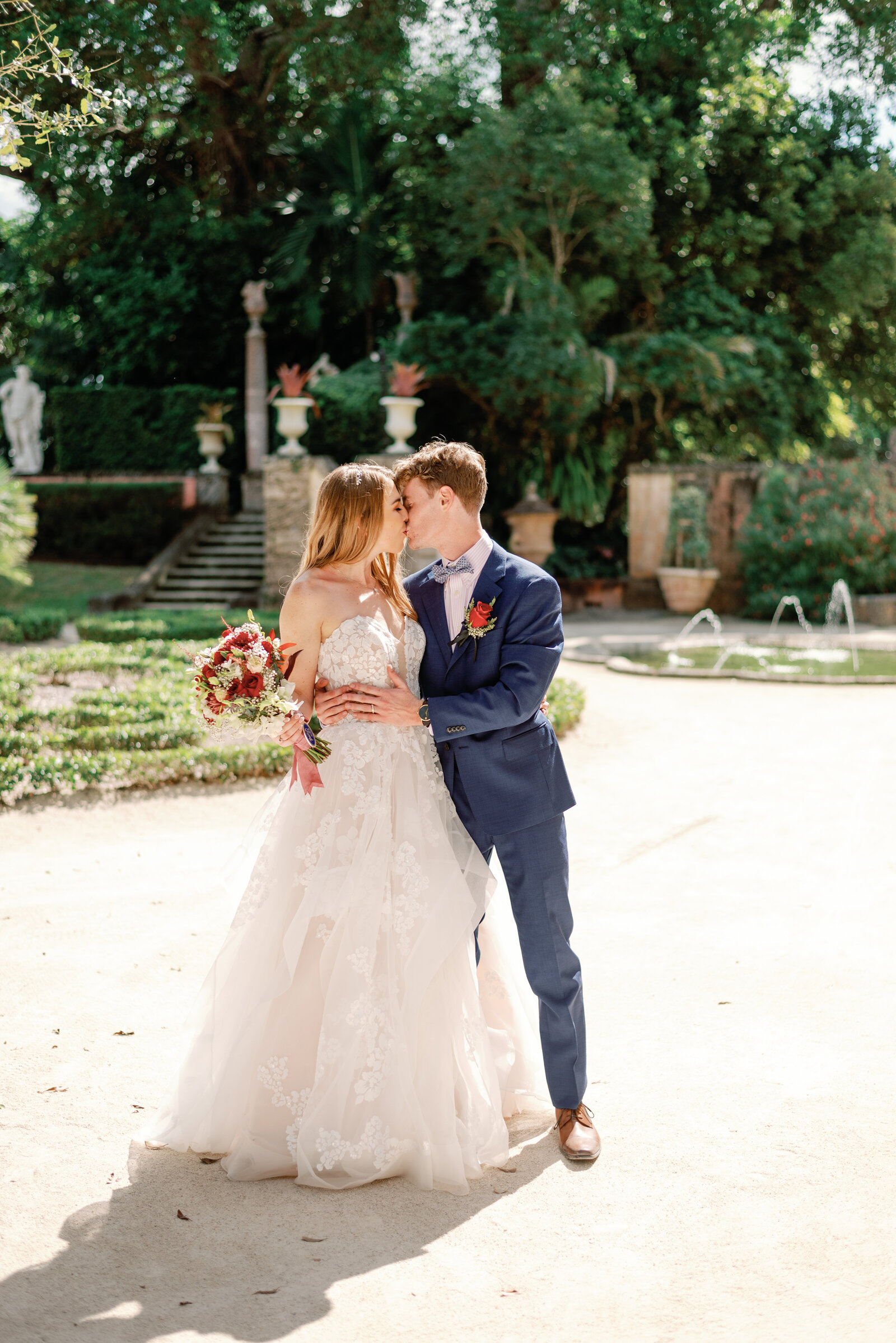 Bride and groom kissing after their wedding ceremony in Vizcaya Garden, sunlight streaming in from slightly behind them