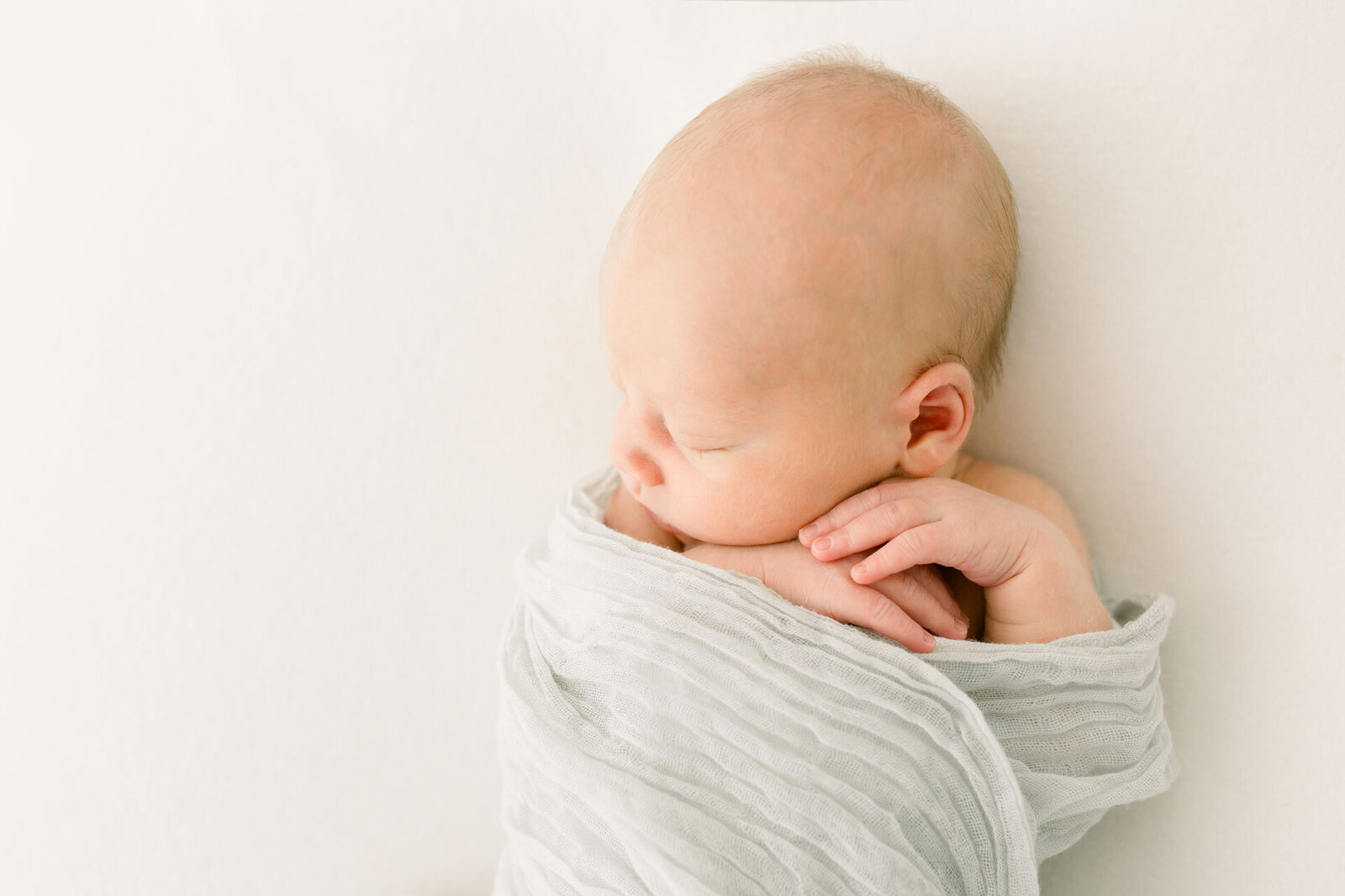Neugeborenenshooting: schlafendes Baby in zarter pastellfarbener Decke.
