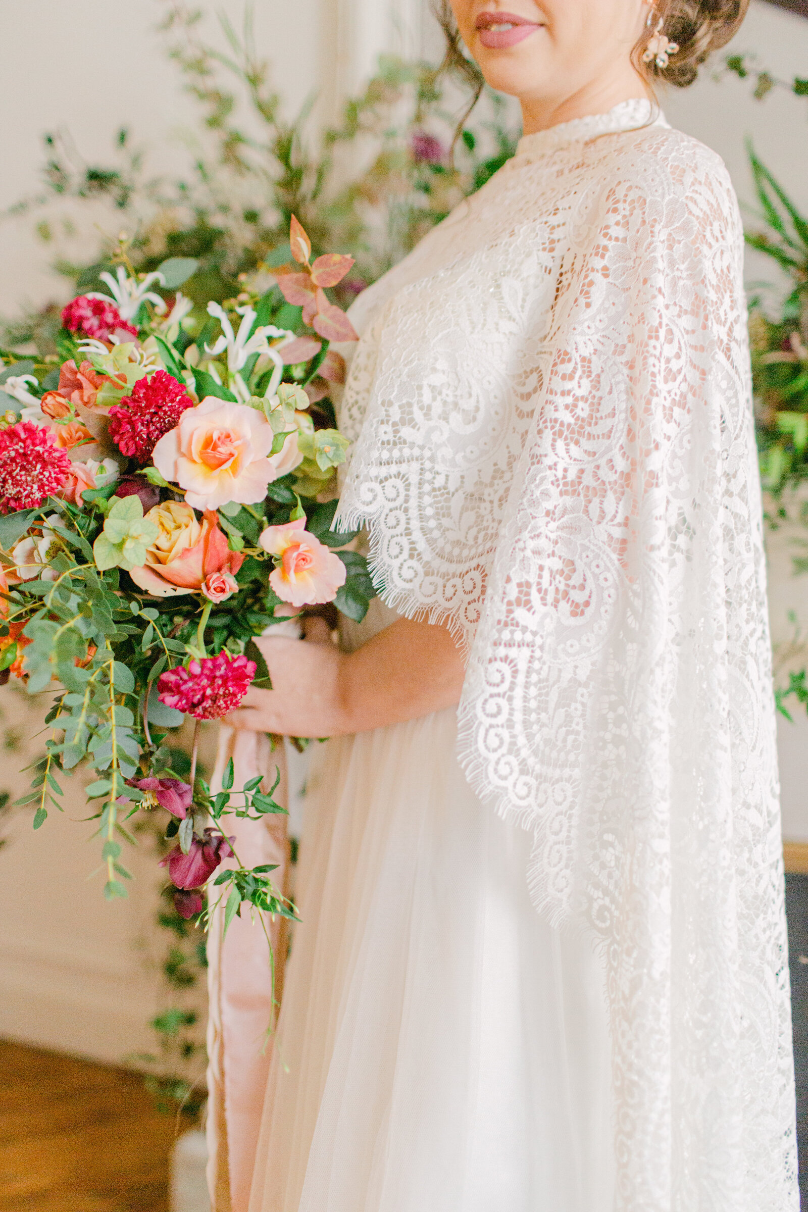bride holding bouquet of flowers wearing a lace cape and standing in front of a fireplace mantel in paris apartment