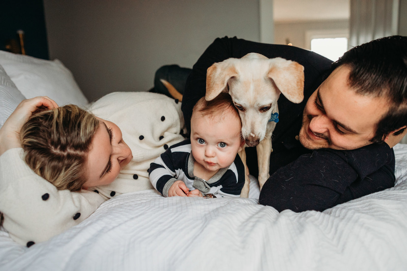 parents snuggle dog and baby on bed