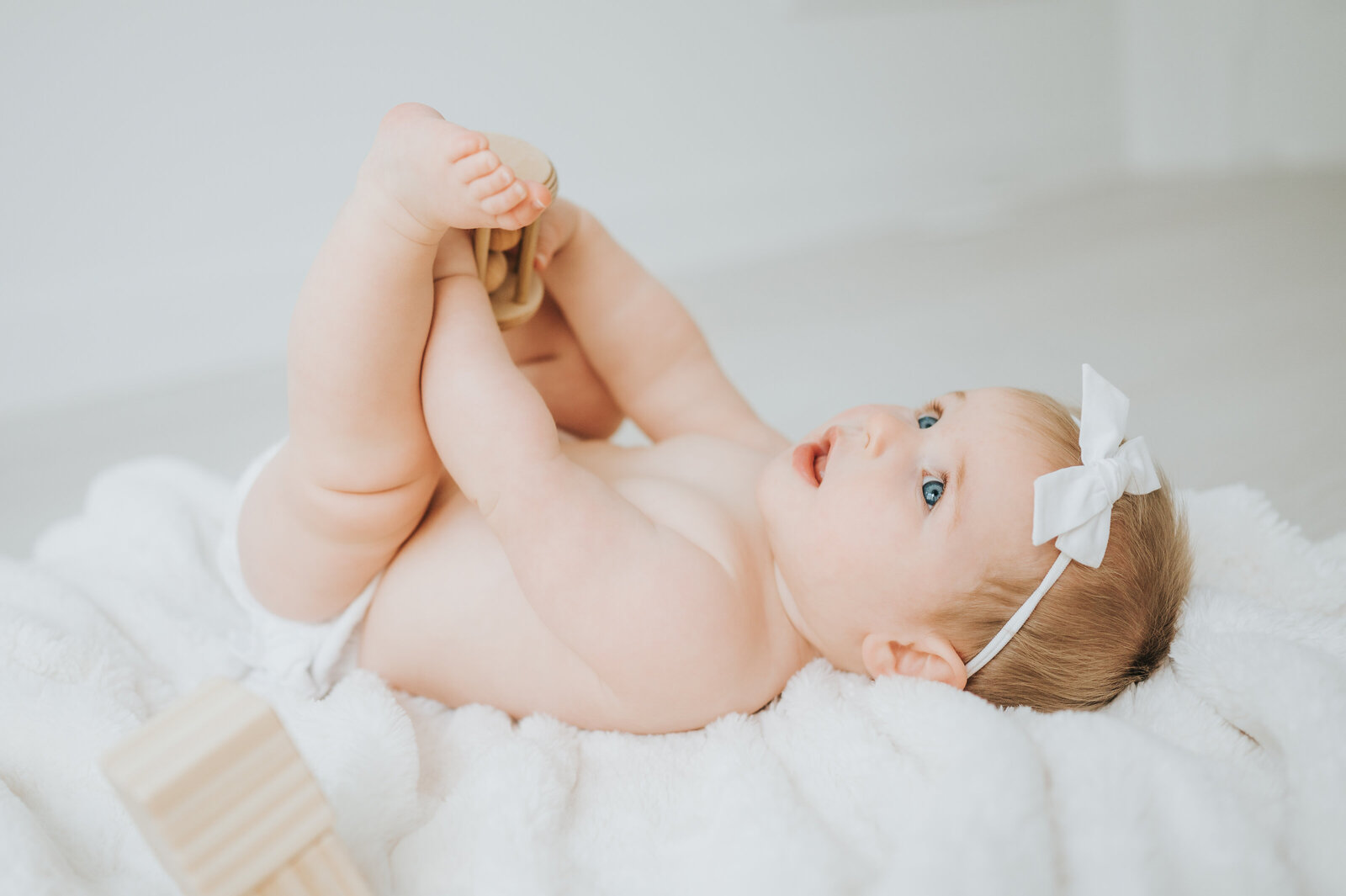 Baby girl lays on her back on white blanket during baby session in Raleigh NC studio
