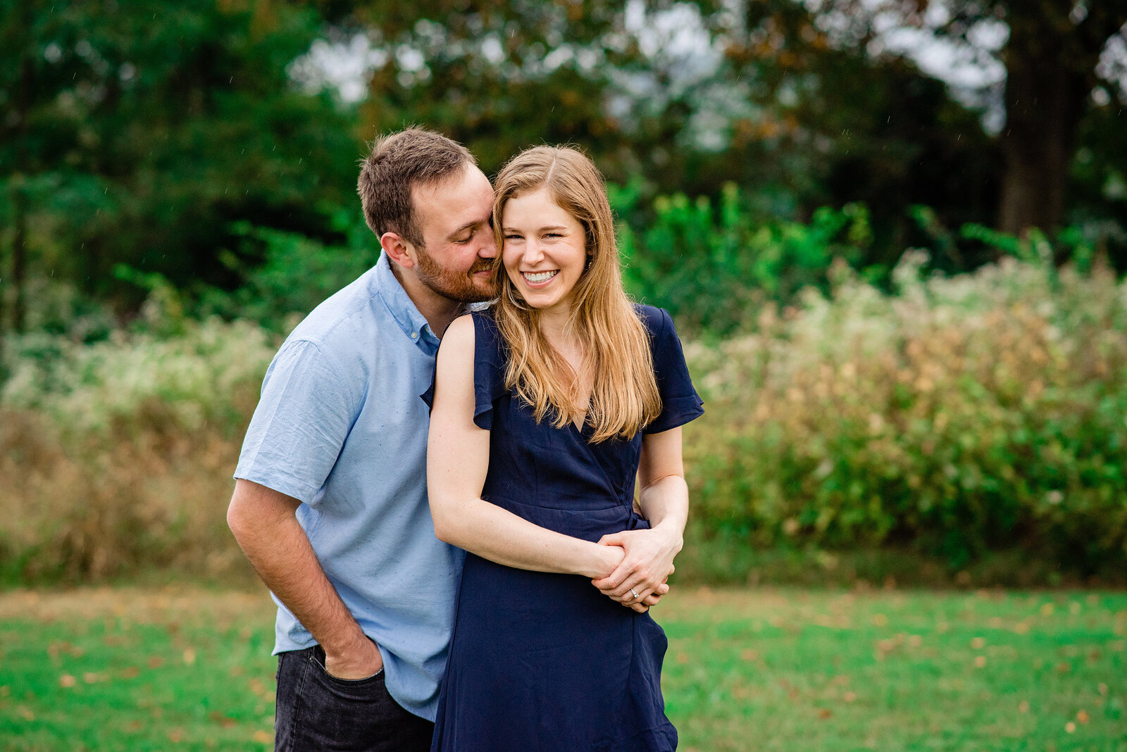 Guy kissing his girls cheek as she smiles and laughs even though it's raining outside