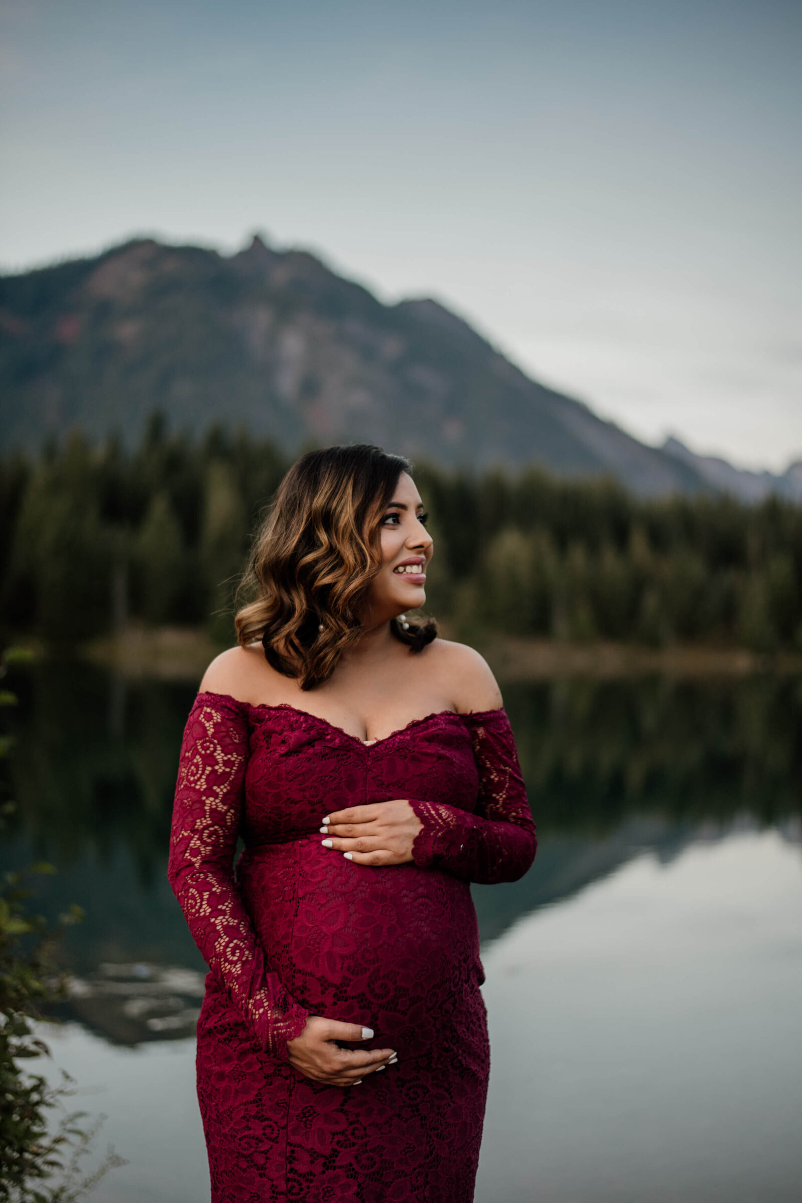 Pregnant woman standing at a forested pond.