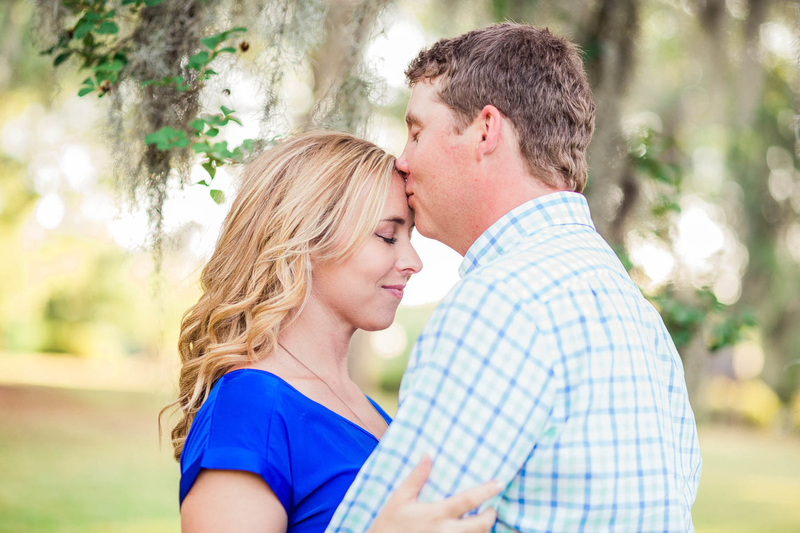 Engaged couple cuddle under a tree with spanish moss, Hampton Park, Charleston Engagement Photography.