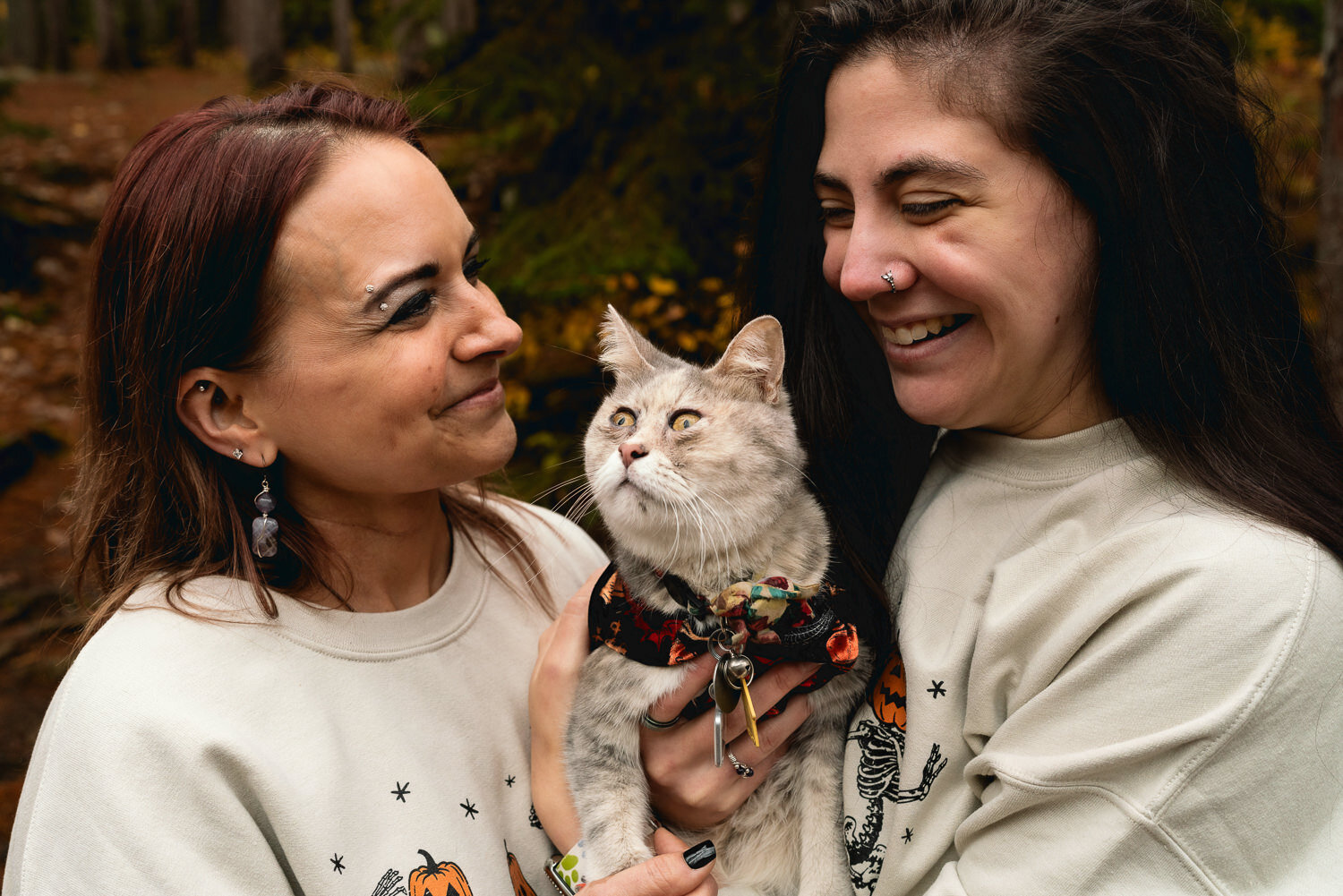 Lesbian couple smile while holding their cat.