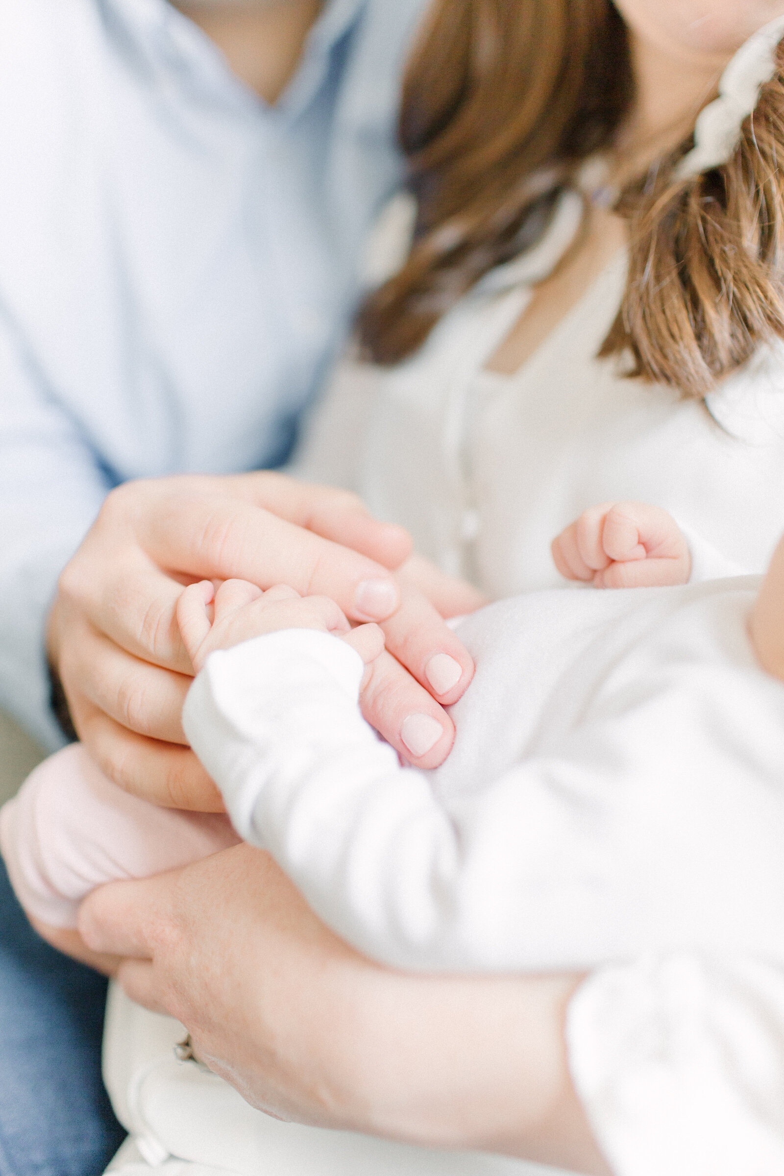 A close up photo of a newborn  baby's hand resting on her parents hands while they hold her