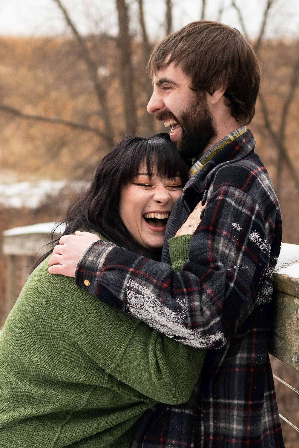 Plus size woman in green sweater laughs while hugging her fiancee.
