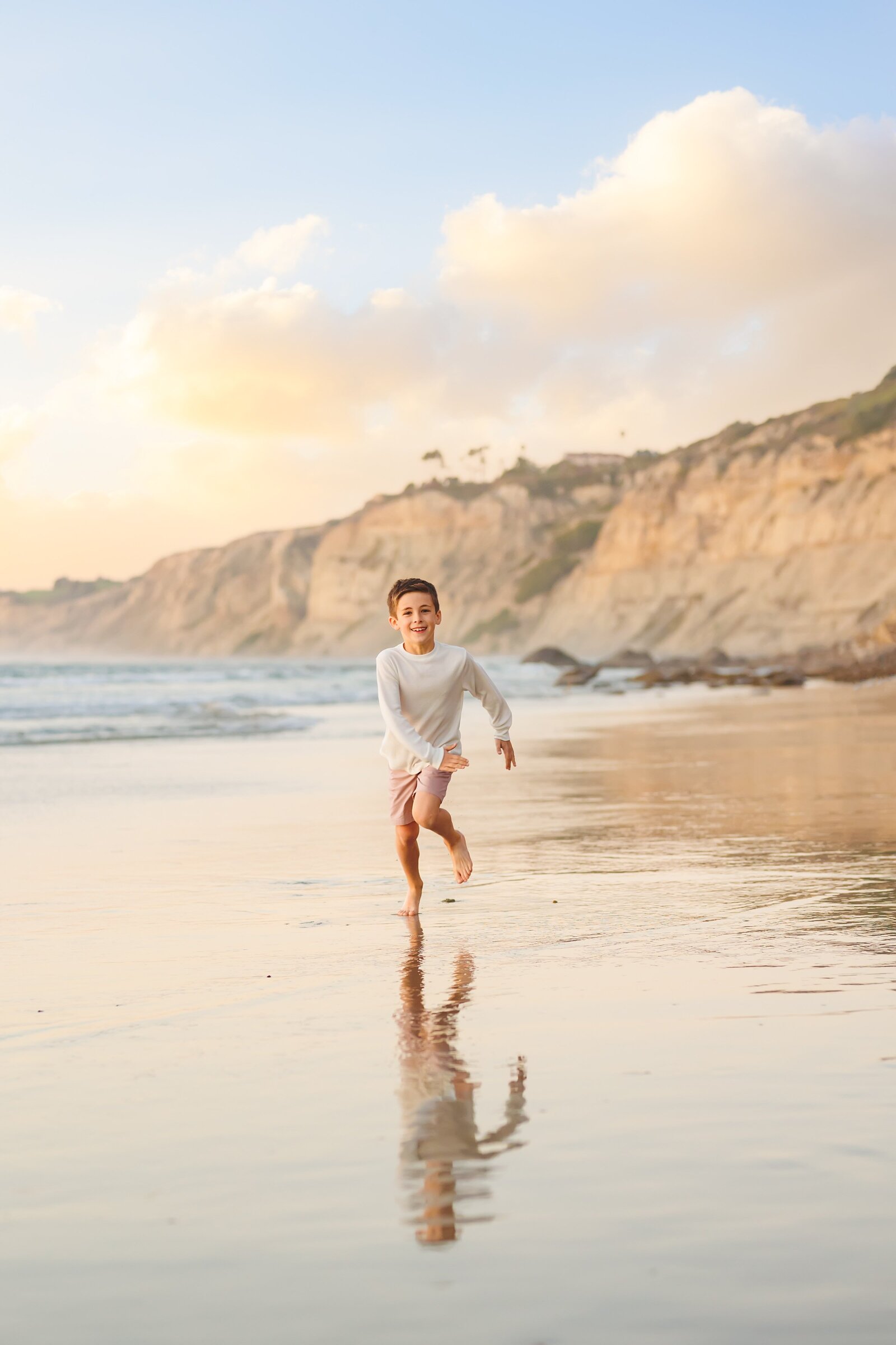 Young boy running on a San Diego beach with his reflection showing on the wet sand