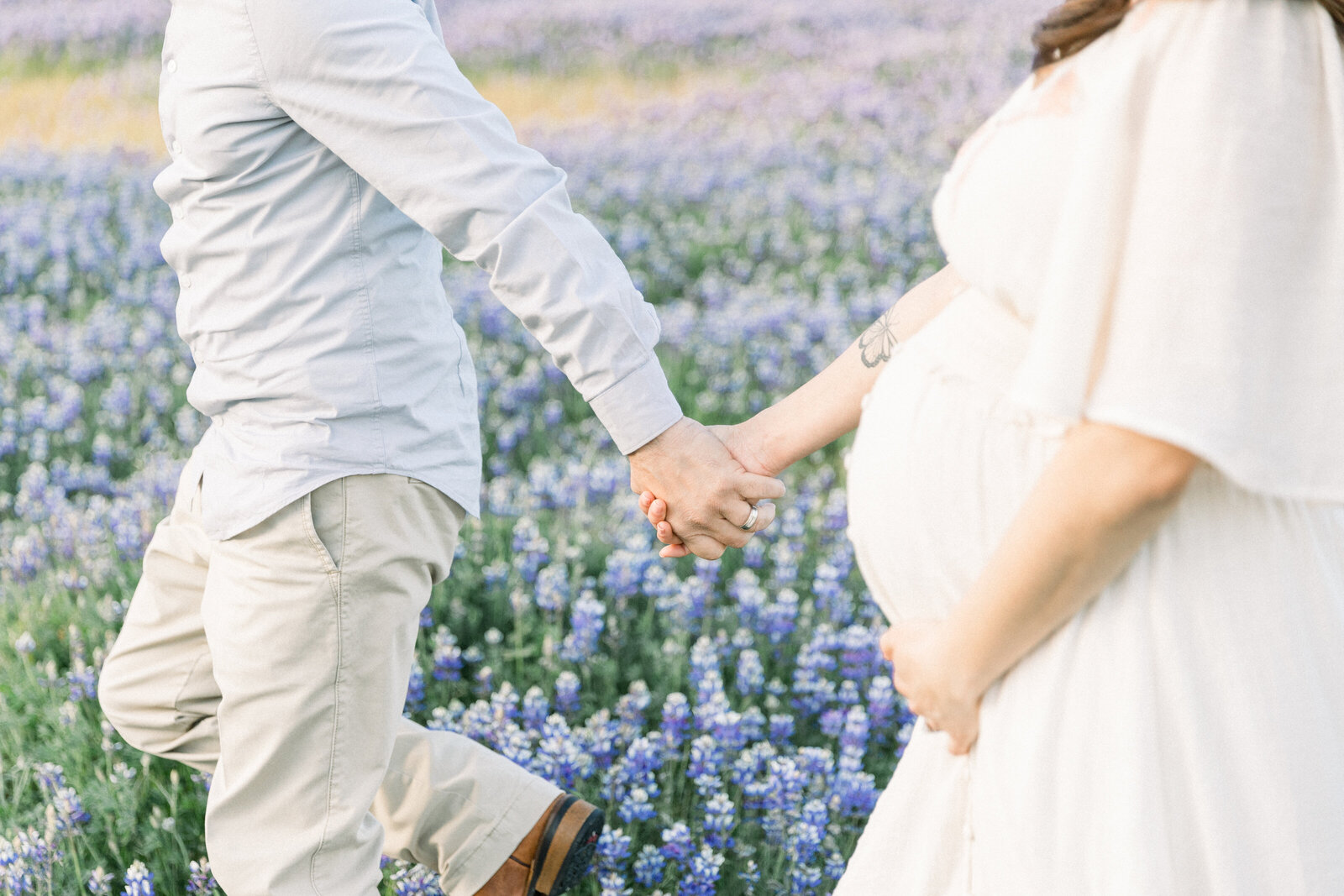 Image of expecting mothers belly holding hands with husband talking through wildflowers taken by Sacramento Maternity Photographer Kelsey Krall
