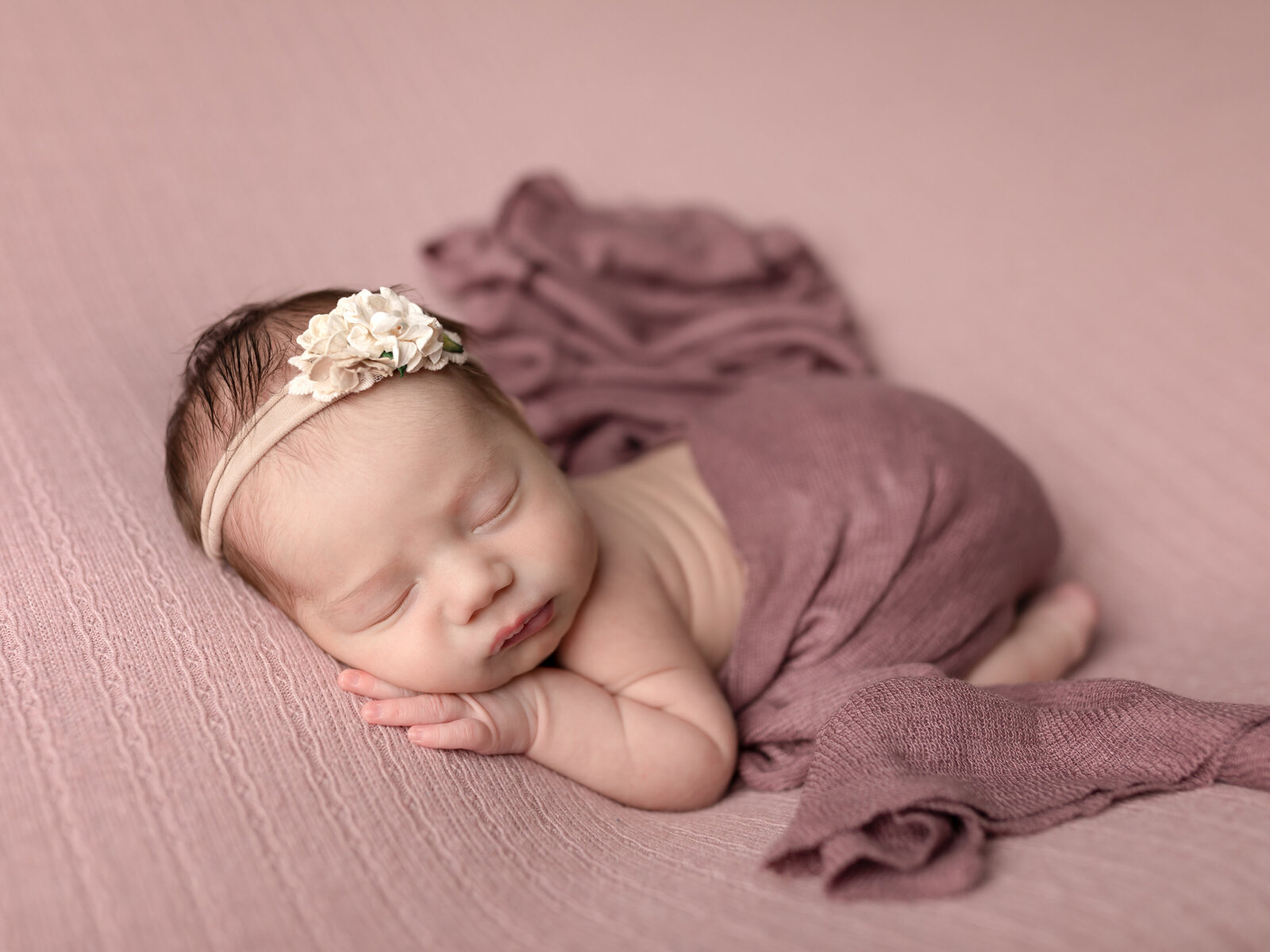 newborn baby girl posed on pink fabric for newborn studio portraits