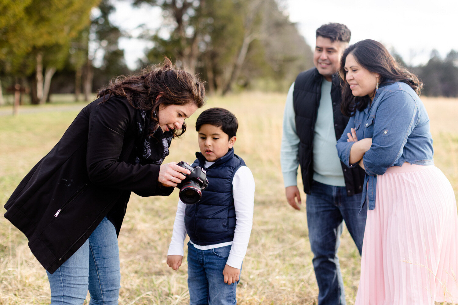 photographer showing child a picture on her camera while the child's parents watch behind him