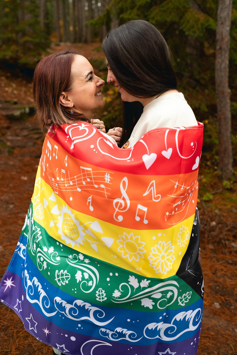 Lesbian couple smiles at each other wrapped in a rainbow flag.