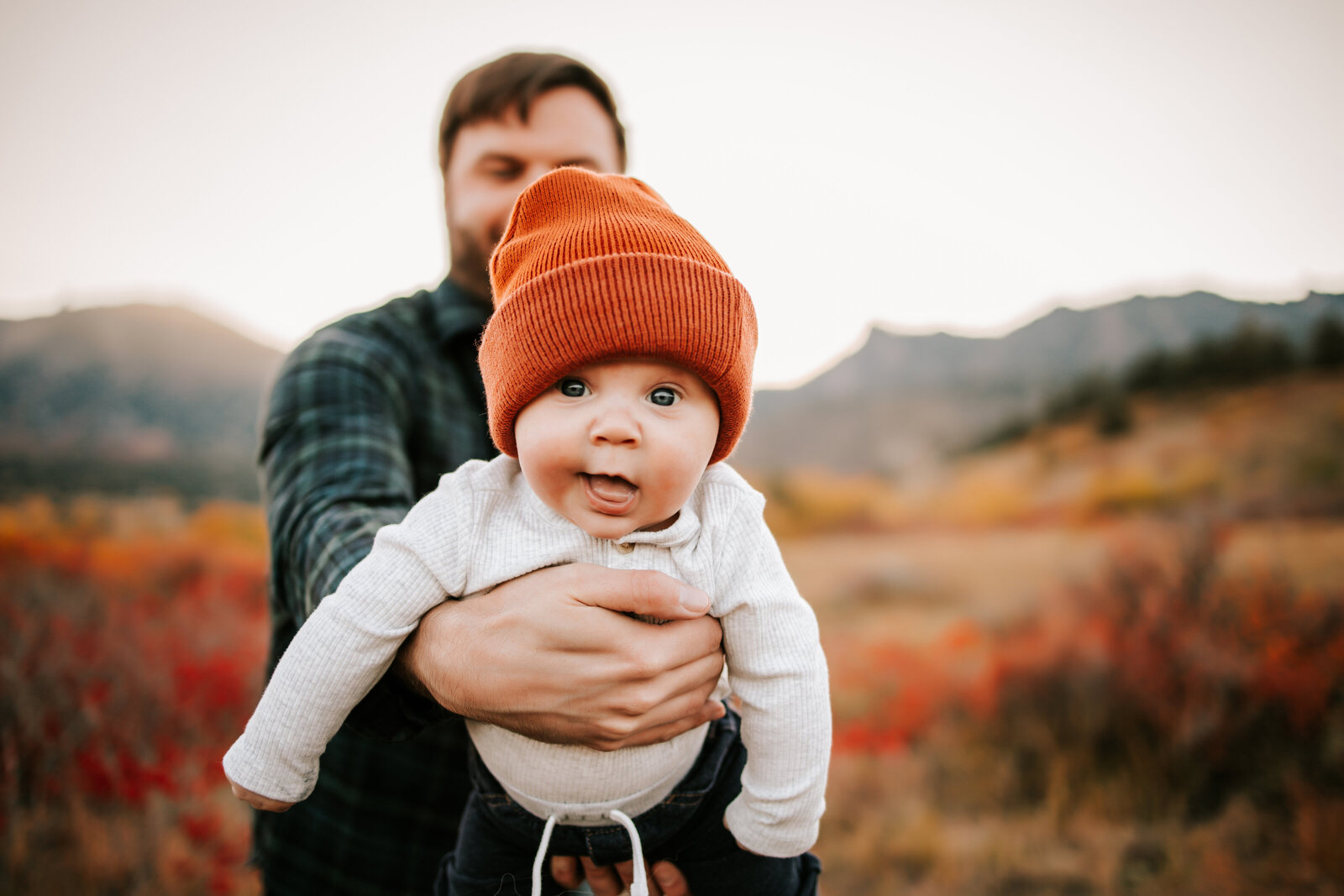 dad holds baby boy  on his belly white wearing an orange beanie