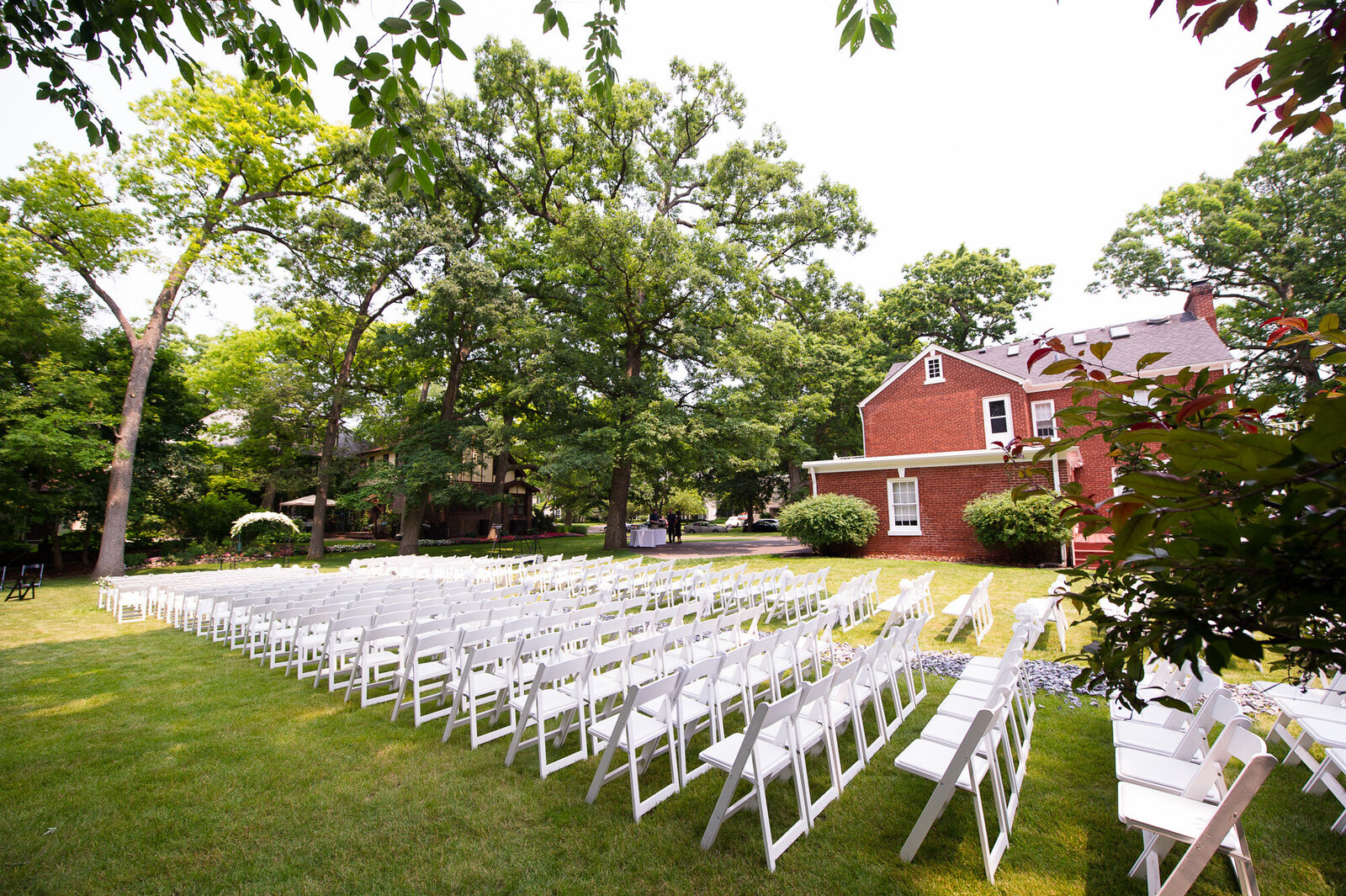 Wedding ceremony site outside with white chairs, trees and a barn