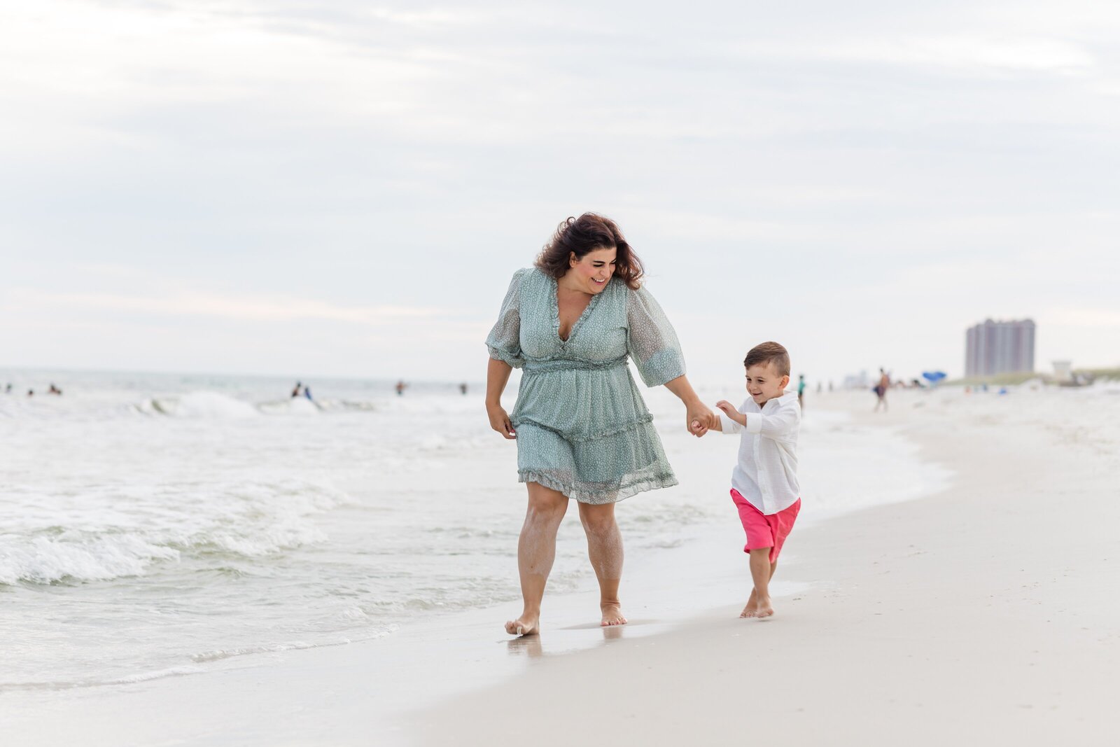 Pensacola Beach vacation family photo session . Mom walking down the beach holding son's hand.