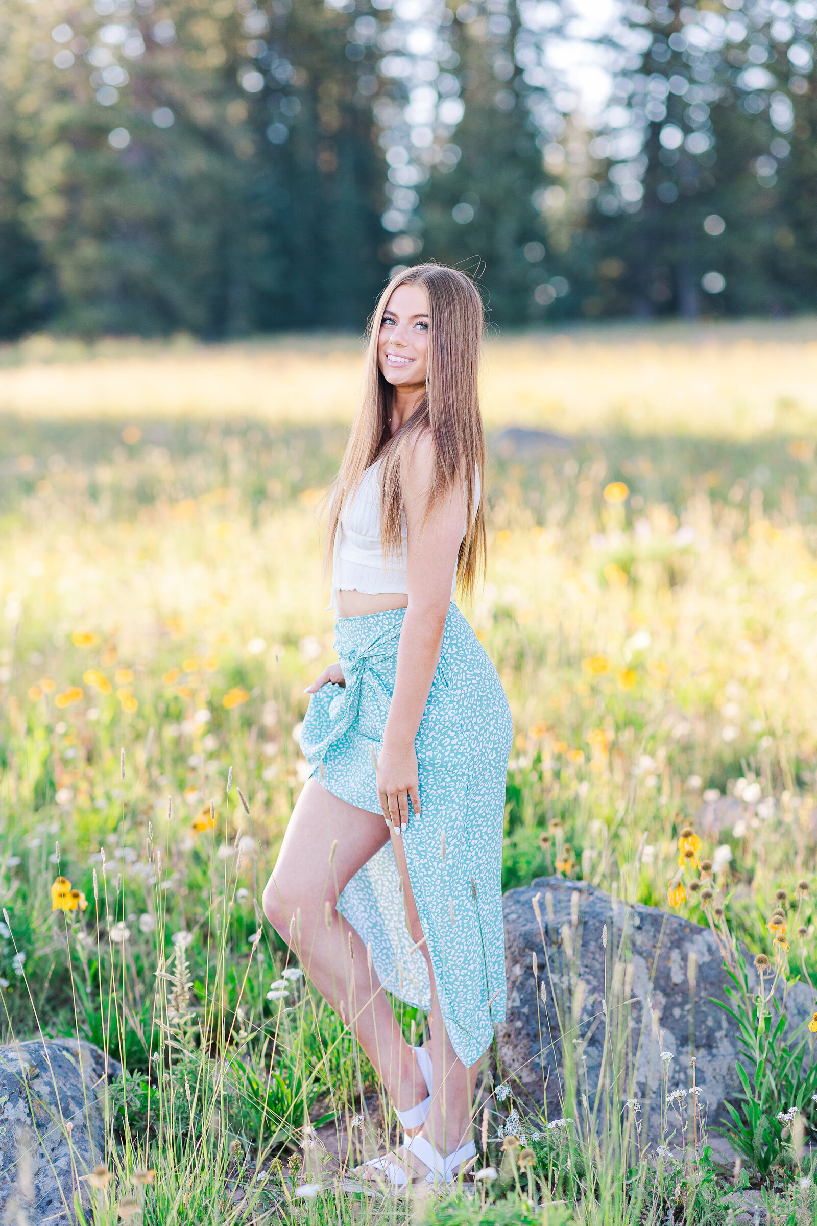 Senior poses in a field of wildflowers in the summer on top of the Grand Mesa