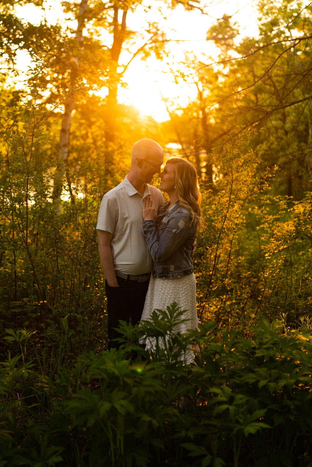 Man and woman in denim jacket smile at sunset in a field.