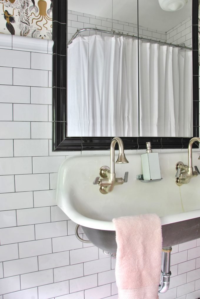 A wallpapered bathroom with subway tile and vintage sink.