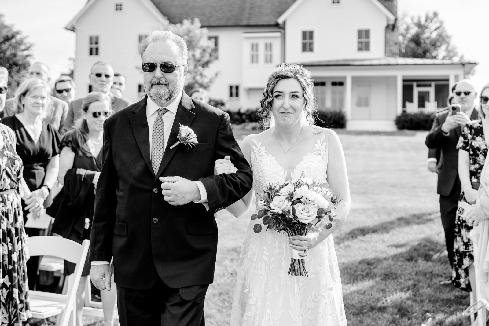 A bride and her father walk down the aisle and the bride is tearing up during her wedding at Blue Hill Farm in Northern Virginia