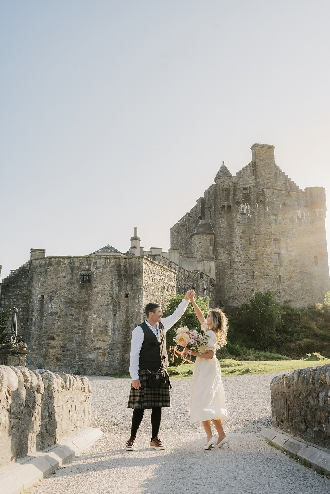 A couple dances joyfully in front of a historic stone castle under a clear sky, capturing the magic you'd find at a photography retreat in New Zealand for creatives and connection.