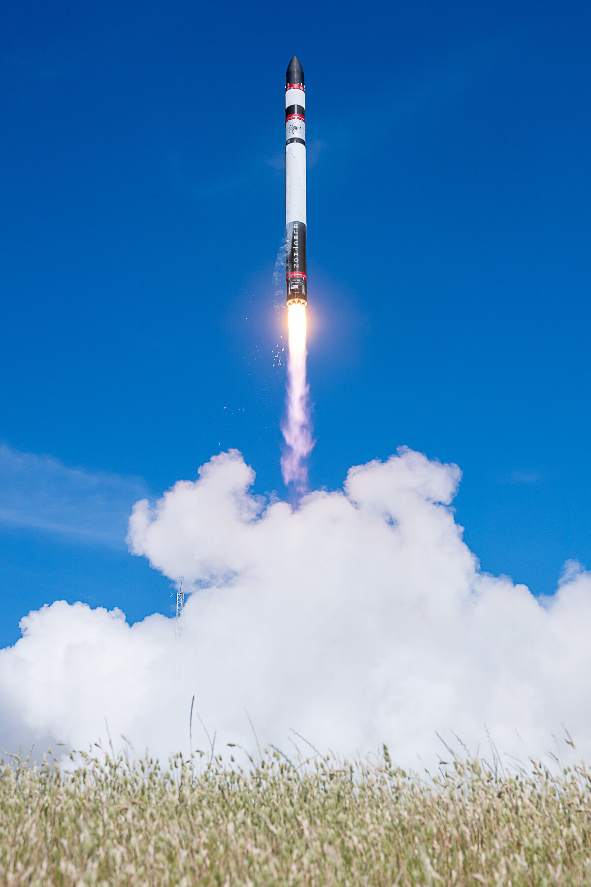 Rocket Lab's Electron rocket launch. Blue sky background  with fire from engines and exhaust smoke below.