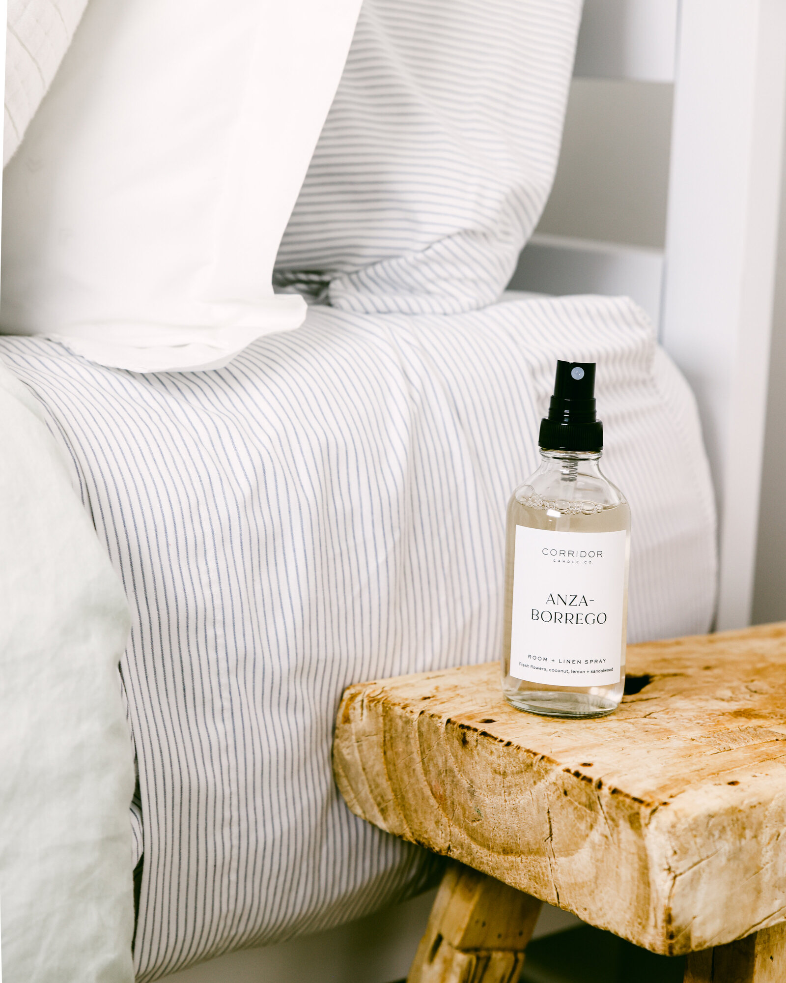 Room spray next to striped bedding rustic bench California product photoshoot
