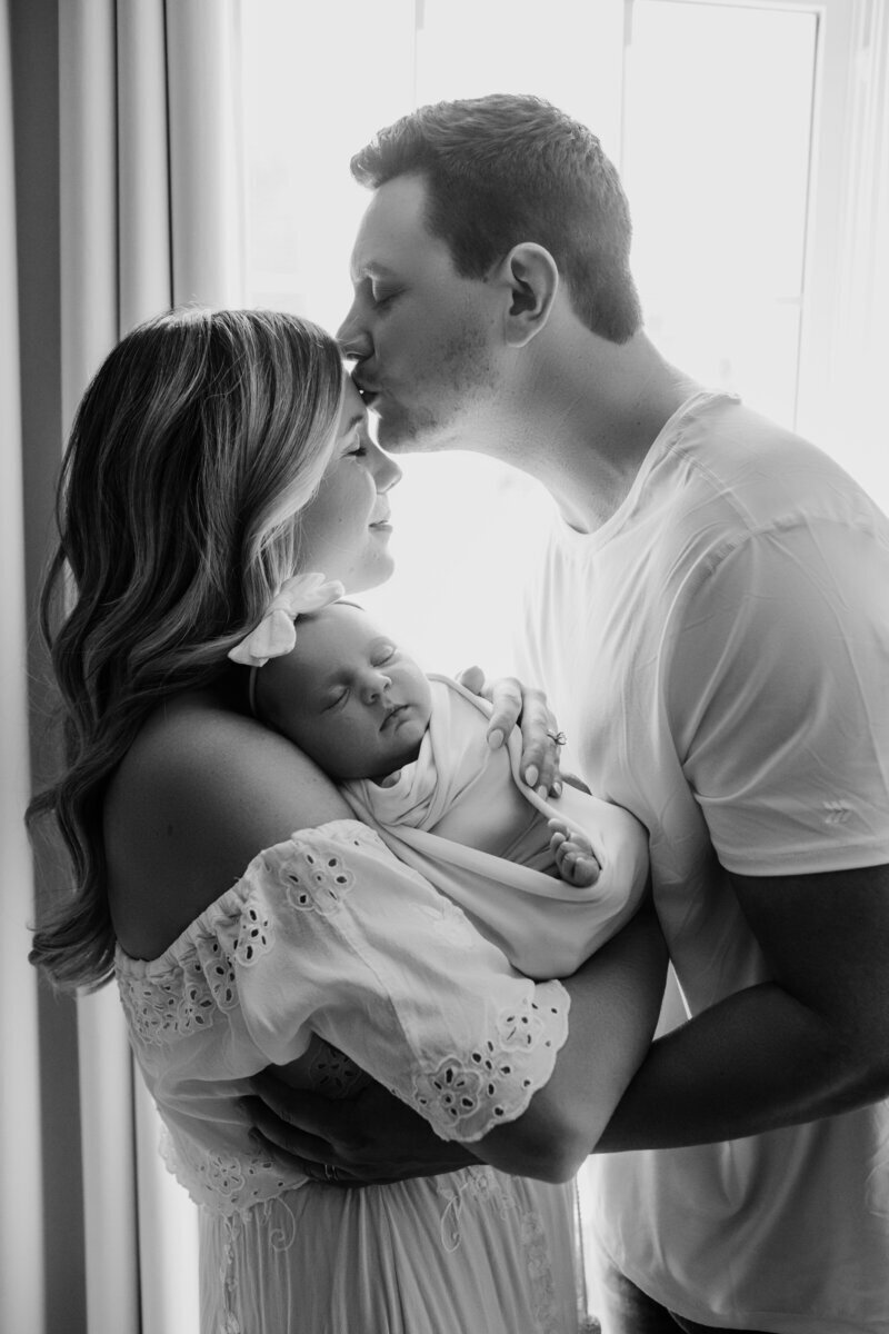 Parents kissing and holding newborn baby in black and white, by best newborn photographers nj
