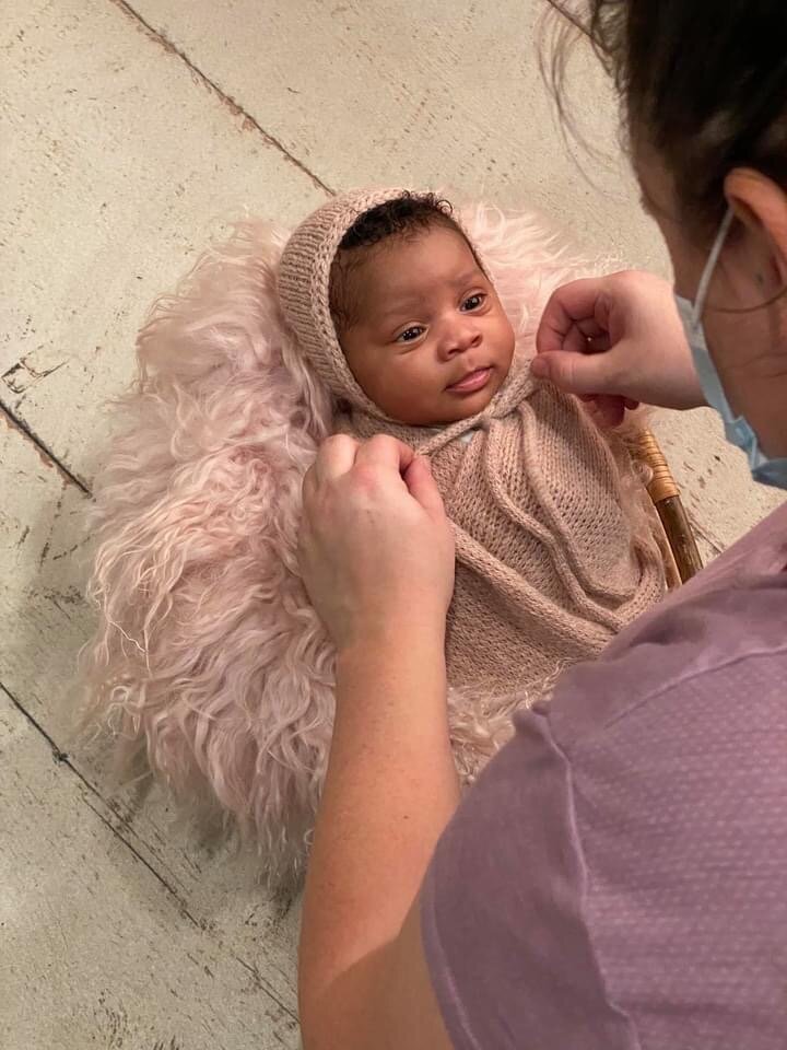 newborn photographer tying bonnet on newborn girl