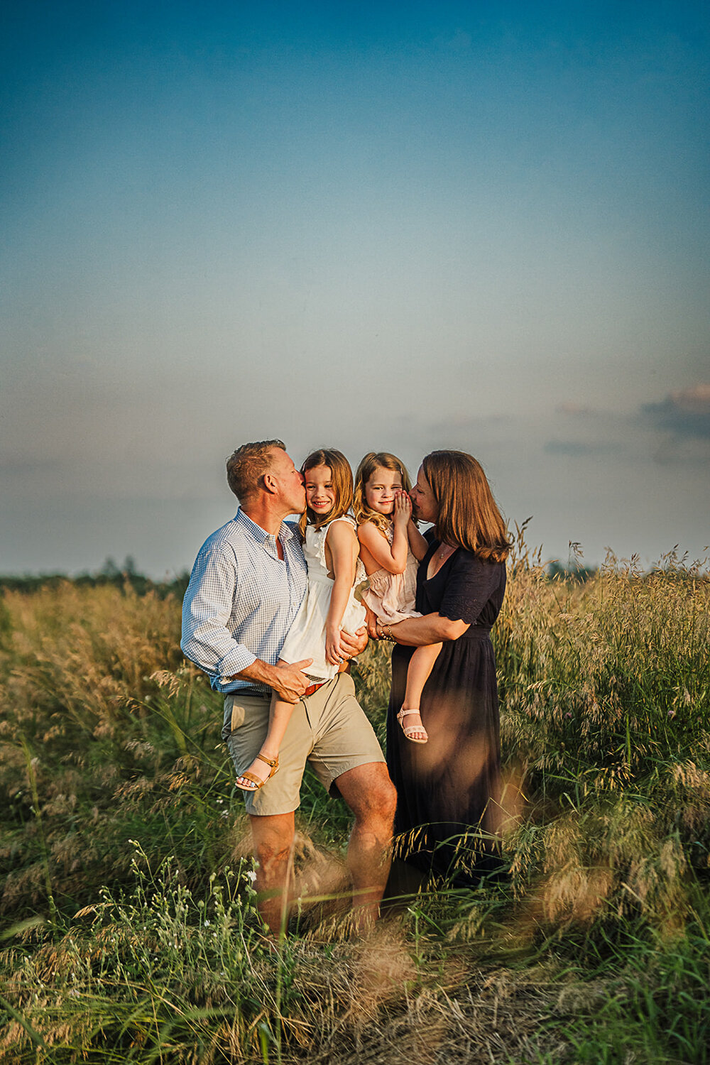 parents stand in a field of wheat at sunset and kiss daughters