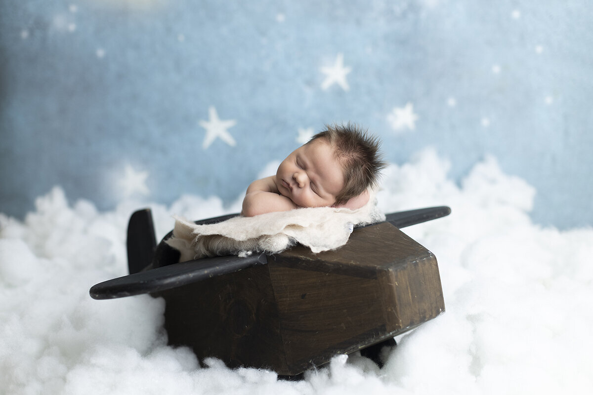 Newborn boy on toy airplane.